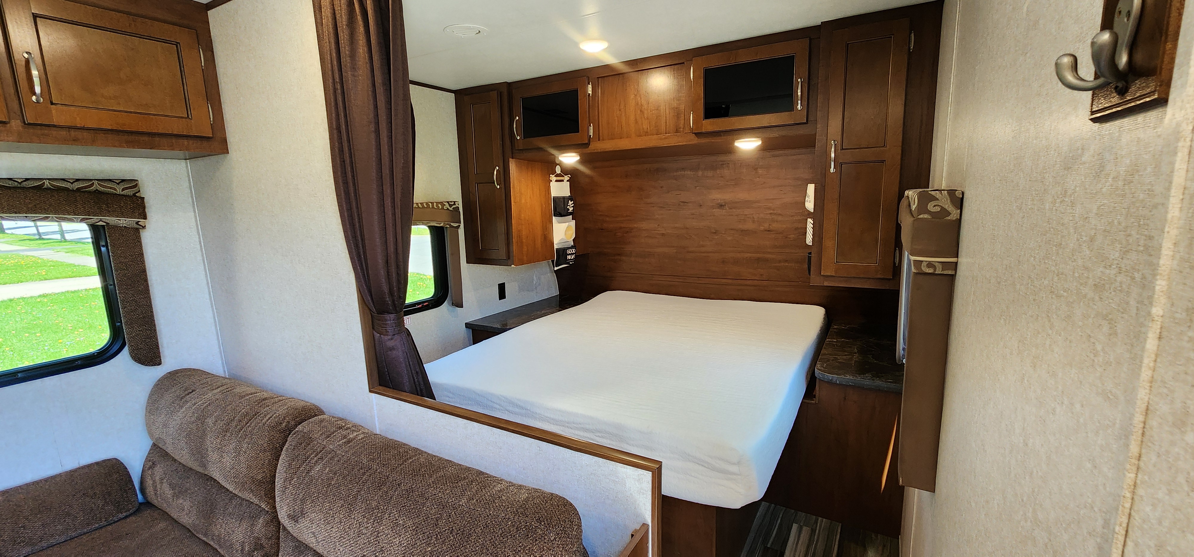This RV rental features a cozy bedroom with a white mattress, rich wood cabinetry, reading lights, and a pull-across privacy curtain.. Jayco Jay Flight 2017