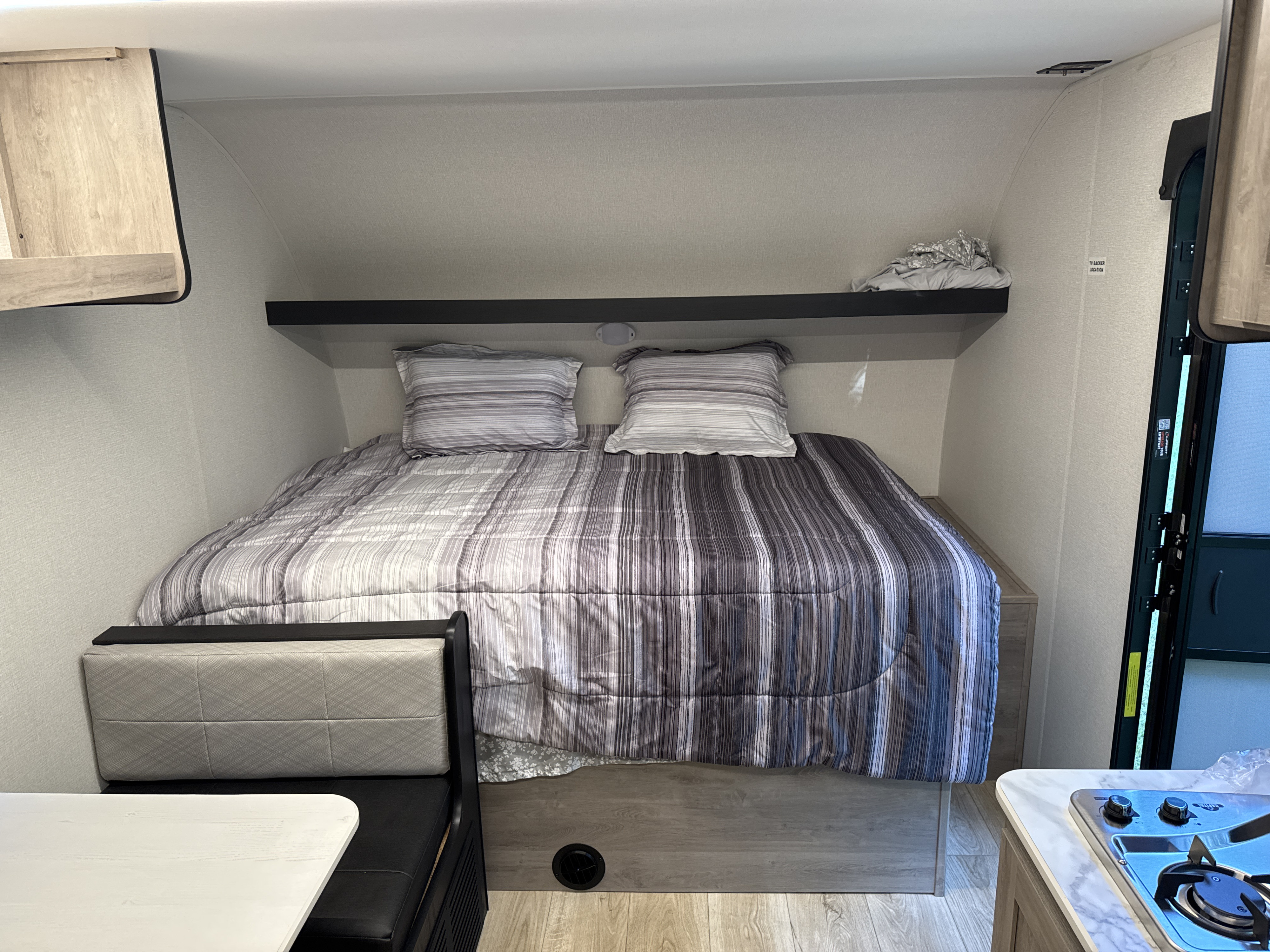 This RV rental shows a compact interior with a striped bed, an overhead shelf, and a dinette area.. Heartland Mallard Mallard 2025