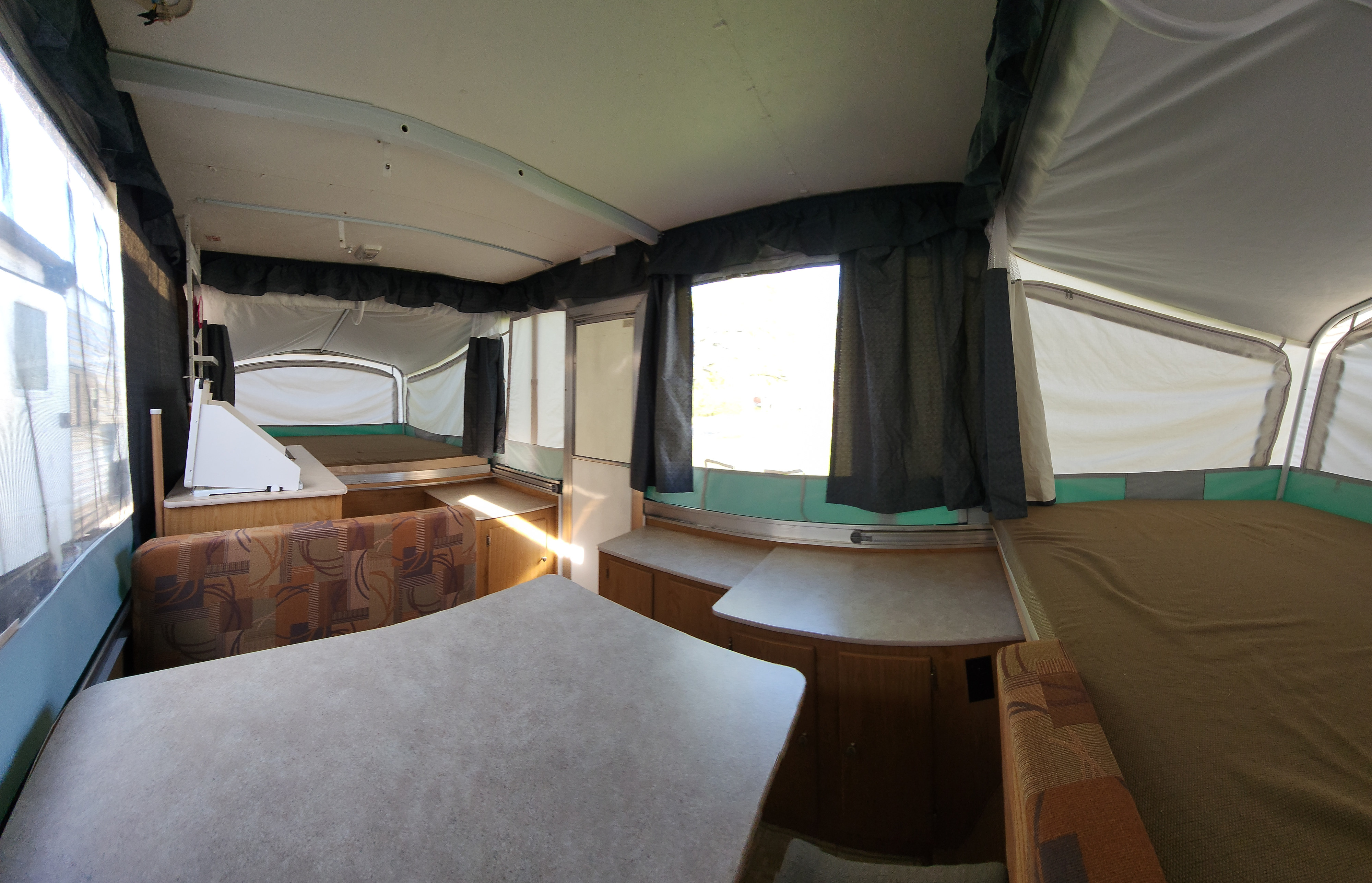 Explore this pop-up camper RV rental interior, featuring a bright dining area with patterned seating and two bed extensions.. Fleetwood Axon 2007