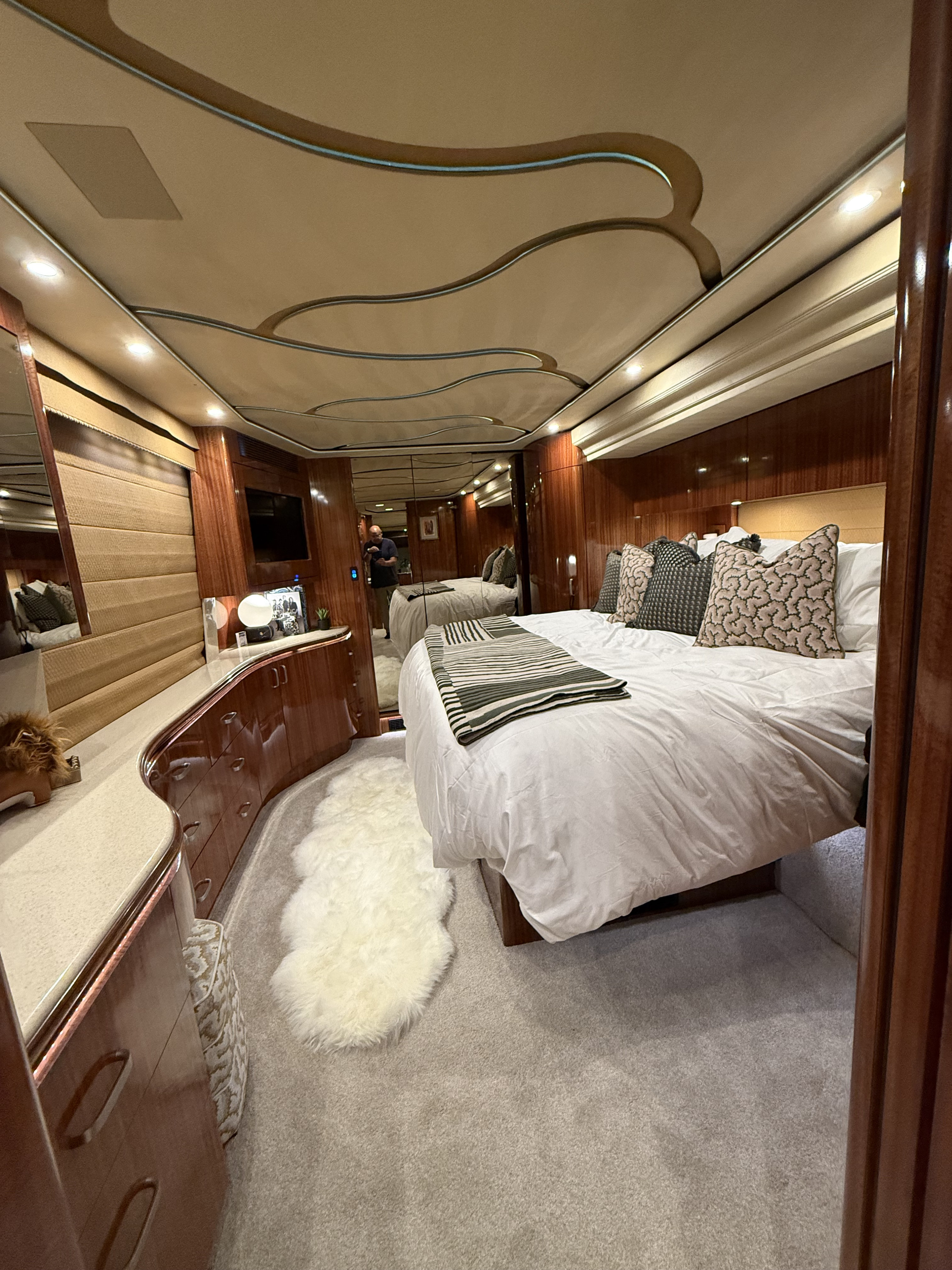 Luxurious RV rental bedroom features a large bed with patterned pillows, polished wood cabinetry, and a cozy rug.. Prevost Marathon 2010