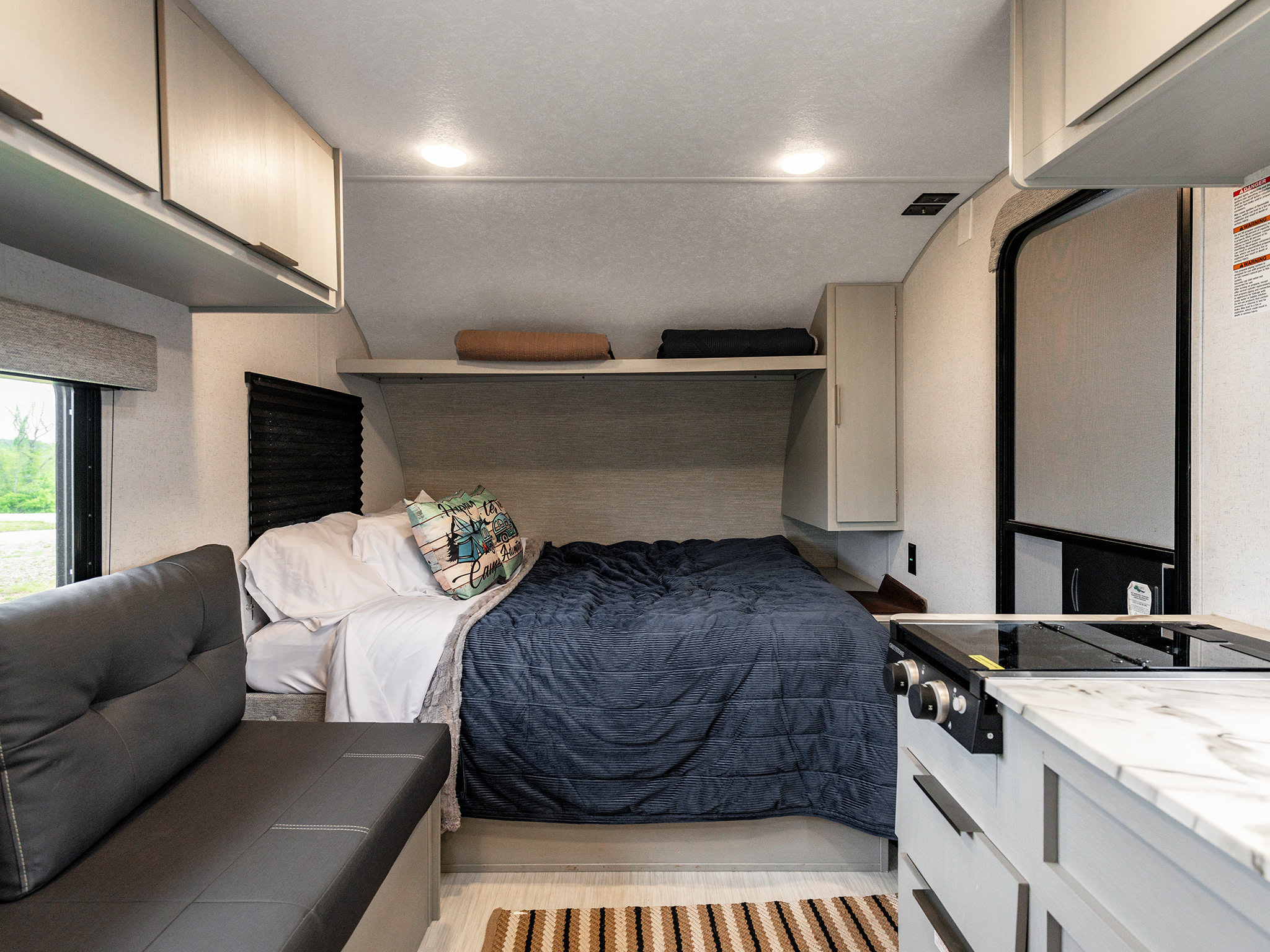 Cozy RV rental interior featuring a comfortable bed, compact kitchen, and sofa seating with overhead storage.. Forest River Salem FSX 2023