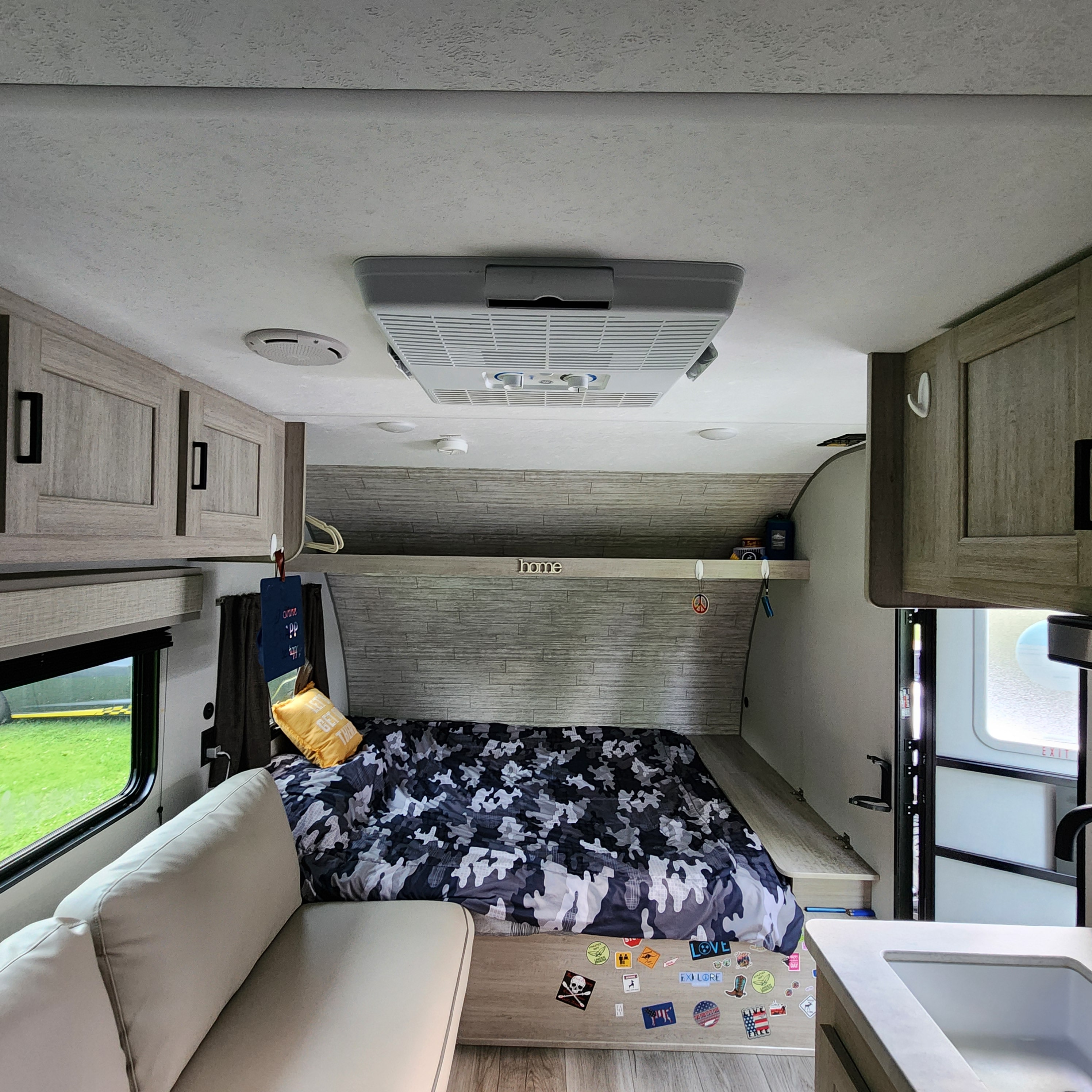 This RV rental interior offers a bed with camo bedding, a comfy sofa, and a small kitchen area, ideal for journeys.. Coachmen Catalina 2024