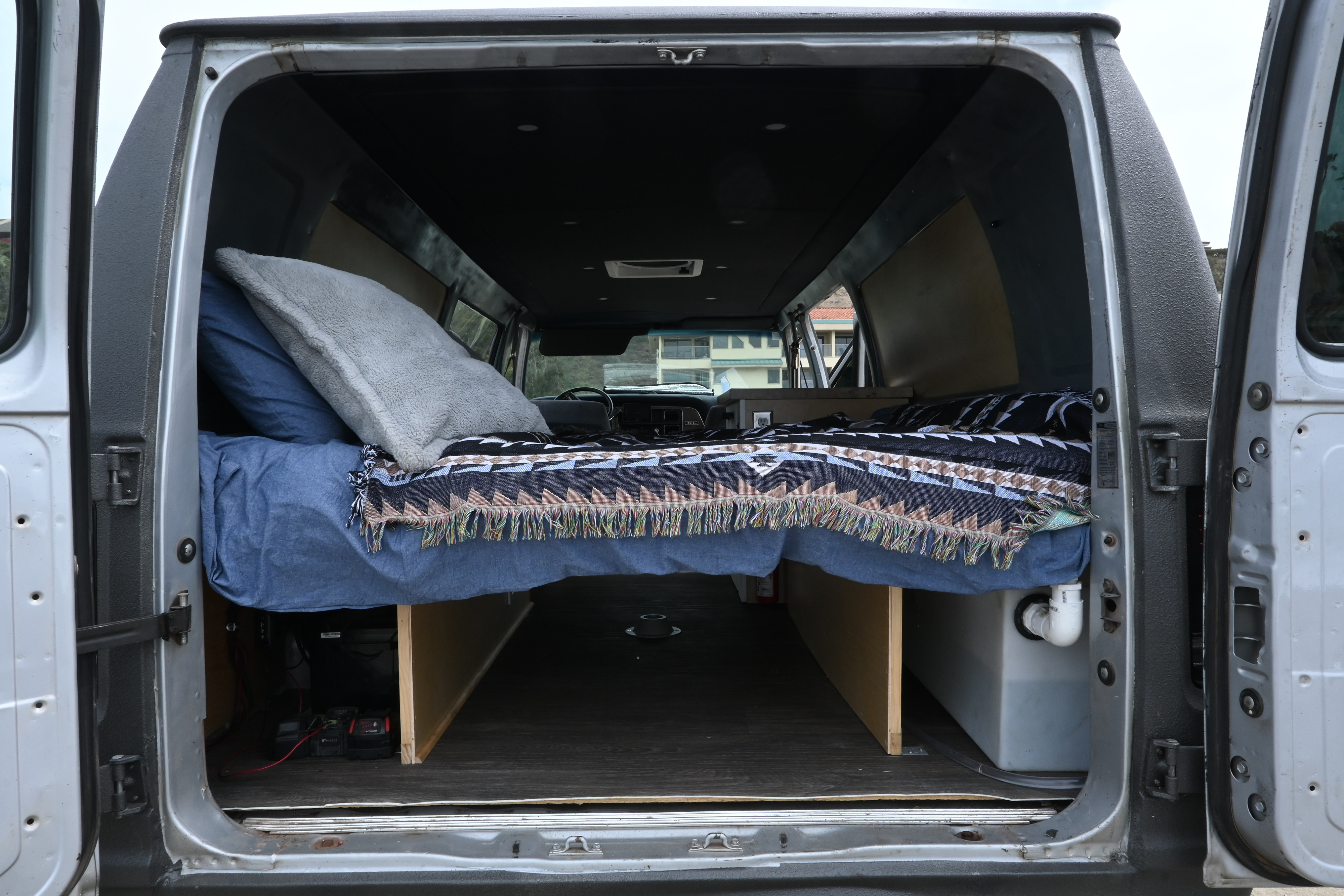 Cozy rv rental camper van interior, seen from the rear doors, showcases a bed, under-bed storage, and custom build details.. Ford Ford E350 1991