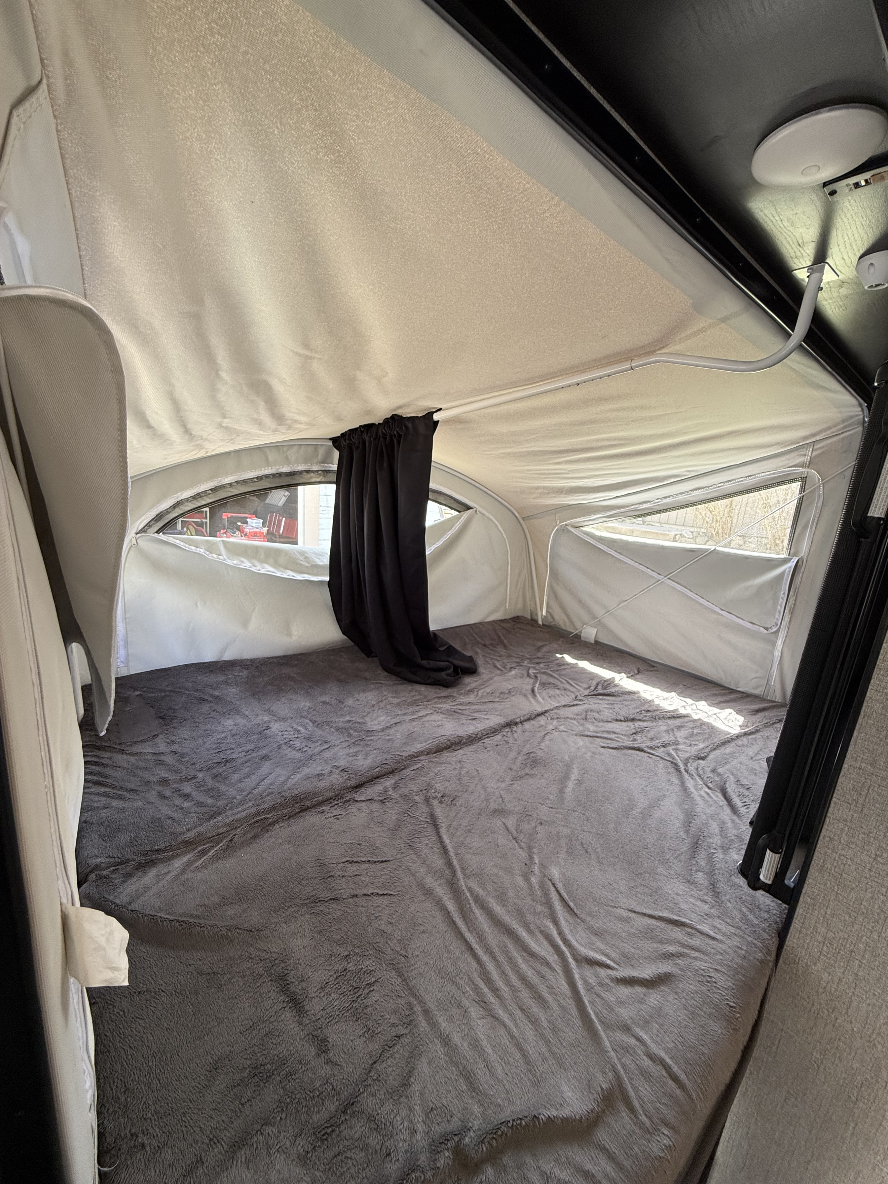 Pop-up RV rental sleeping area features a large grey blanket, canvas walls, and ample windows for light.. Jayco Jay Feather 2021