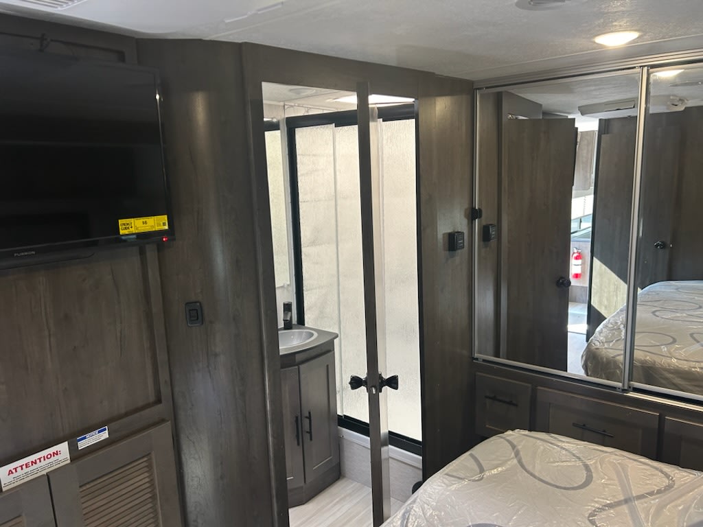 RV rental bedroom with TV, mirrored closet, and a compact bathroom featuring a sink & shower.. Forest River Coachmen Leprechaun 2023