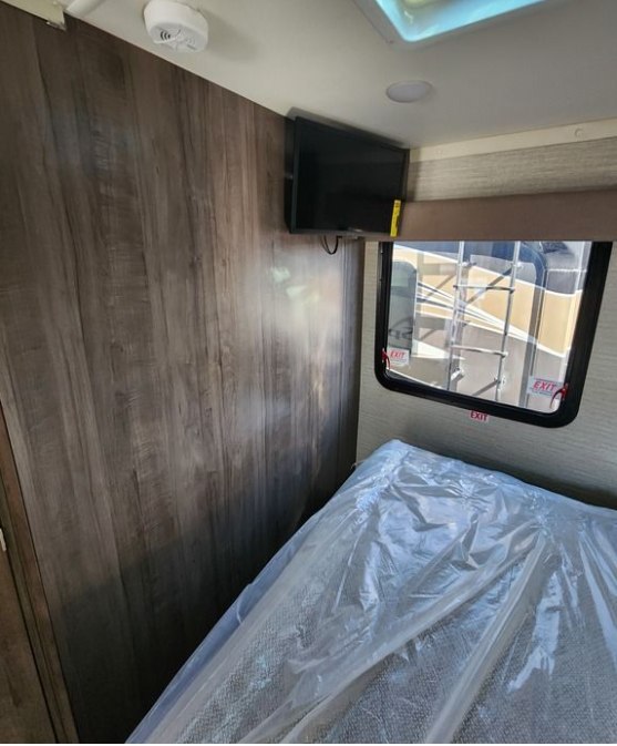 Compact **RV rental** interior: Bedroom features a plastic-covered bed, wall-mounted TV, window, and wood-paneled walls.. Winnebago Spirit 2024
