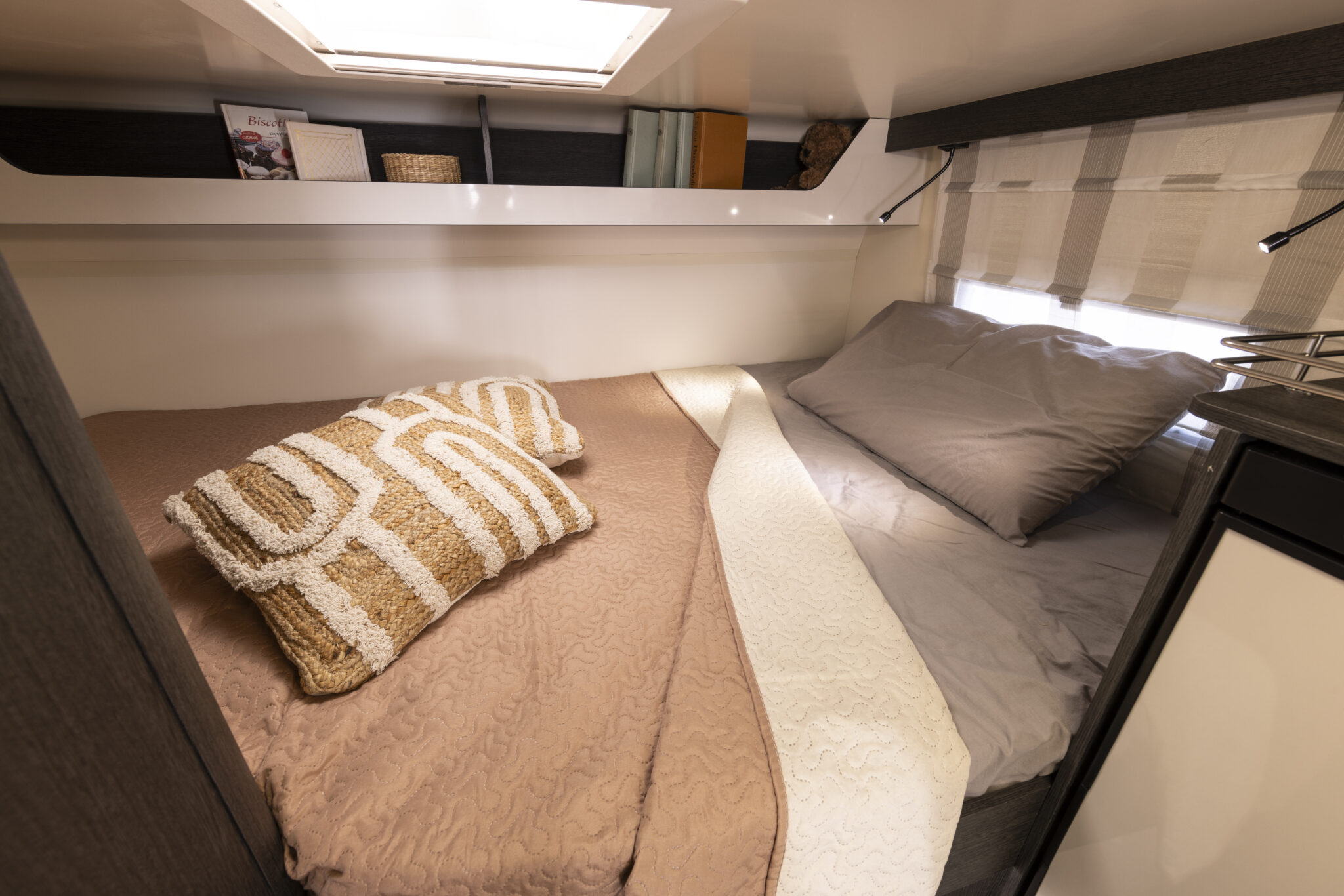 Inside an RV rental: a comfortable bedroom with soft pillows, reading lights, and overhead storage. Ideal for travel.. Rollerteam 675 2022