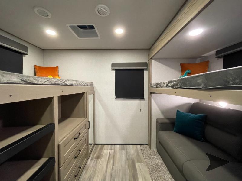 Modern RV rental bunkhouse with multiple comfortable bunk beds, a sofa, and integrated storage, well-lit for travelers.. Grand Design Reflection 2024