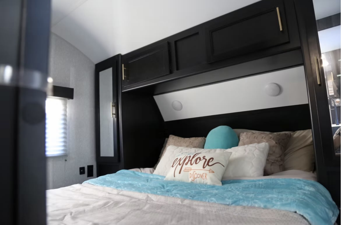 Experience comfort in this RV rental bedroom, showing a large bed with a blue blanket and sleek black overhead storage.. Forest River Cherokee Grey Wolf 2022