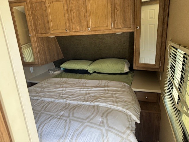 An RV rental's cozy bedroom with a bed, green pillows, overhead cabinets, and mirrored storage.. Forest River Shasta Revere 2016