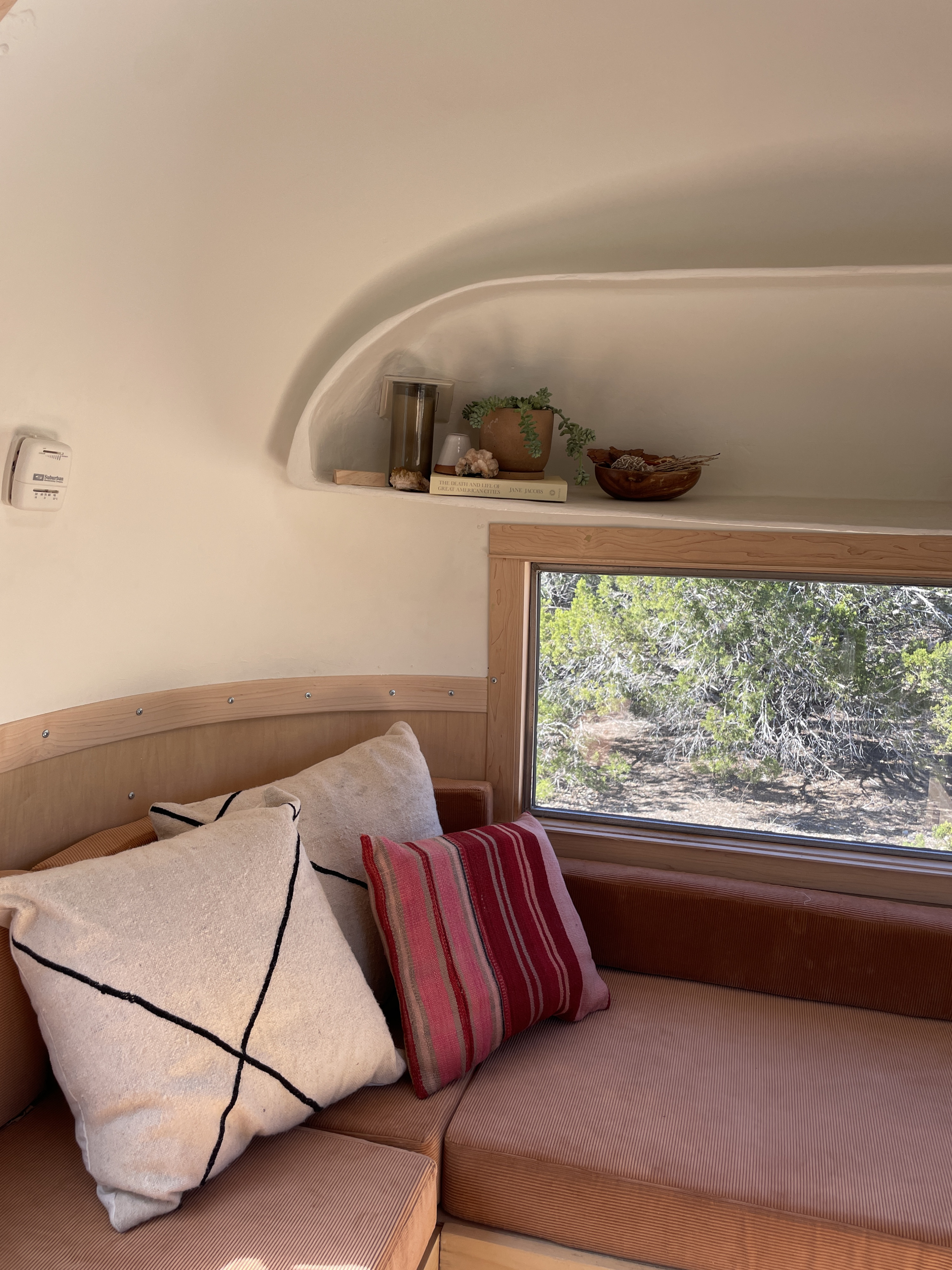 Cozy RV rental interior with plush seating, natural wood accents, and a built-in shelf displaying plants & decor. Enjoy the view!. Airstream Safari 1964