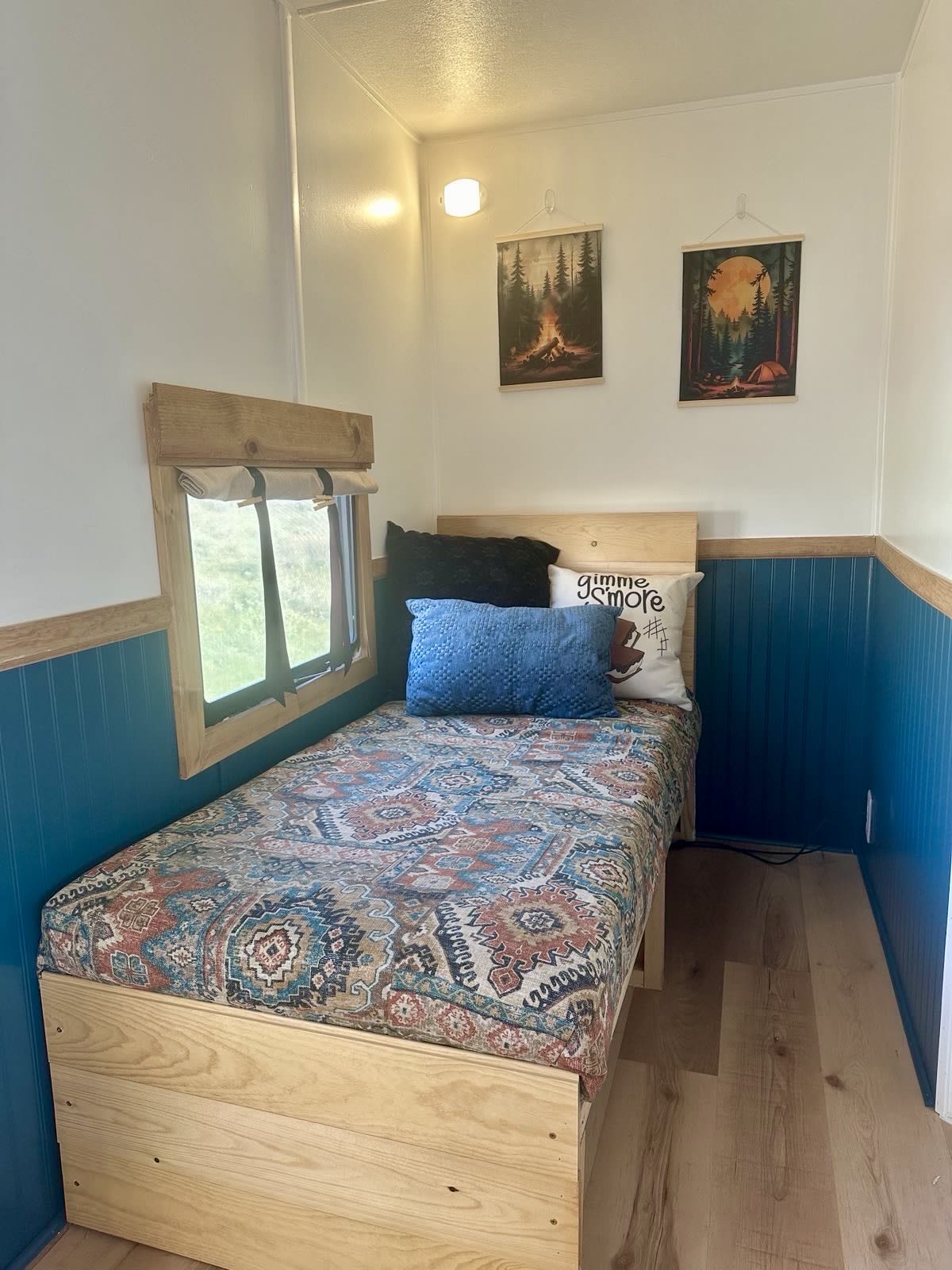 Cozy single bed in an RV rental, featuring camping decor, a window, and blue wainscoting.. Heartland RVs Prowler 2022