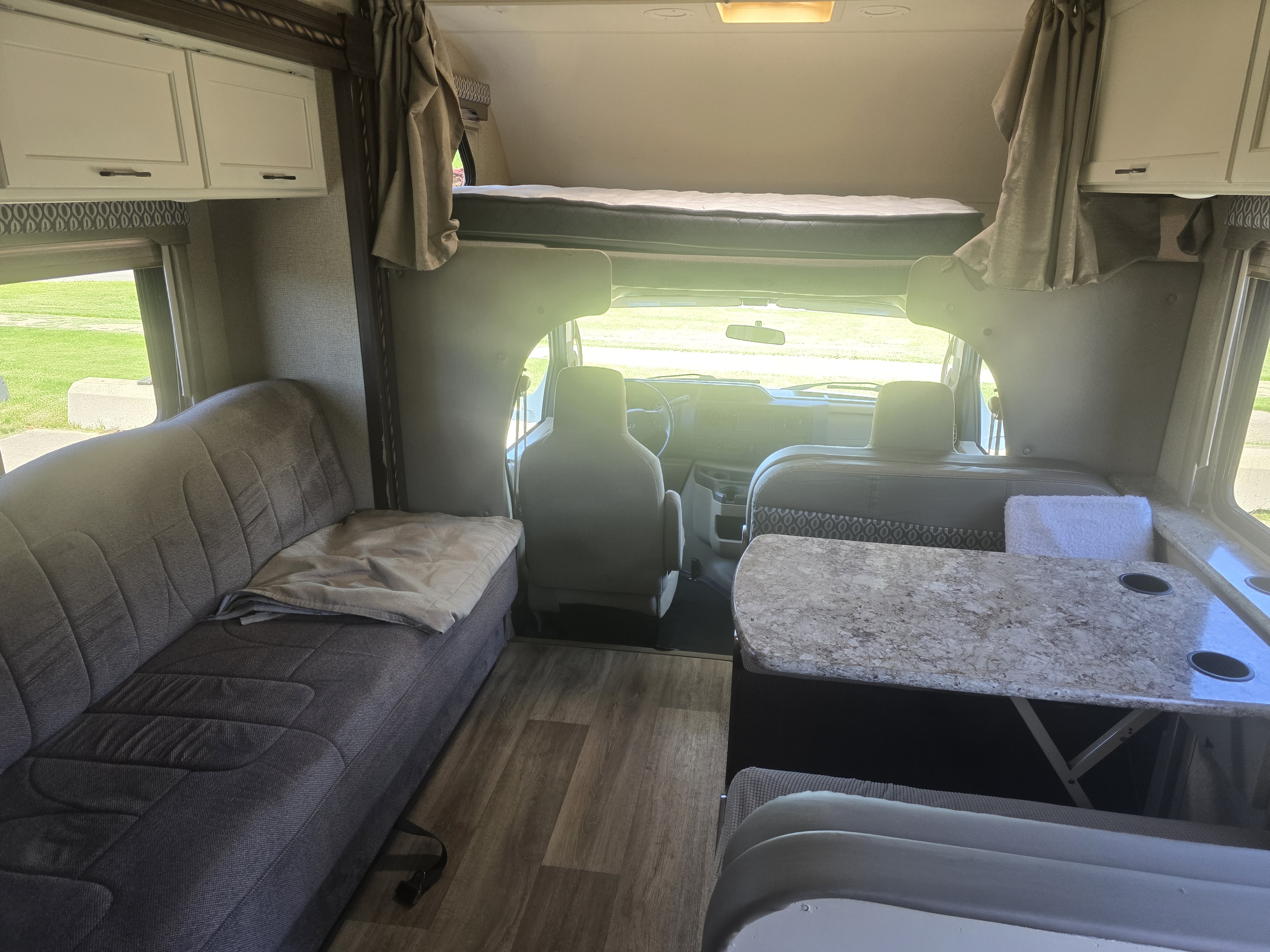 Inside a modern RV rental, featuring a lounge area, overhead bunk, and a dining table with cup holders.. Thor Freedom Elite 2017
