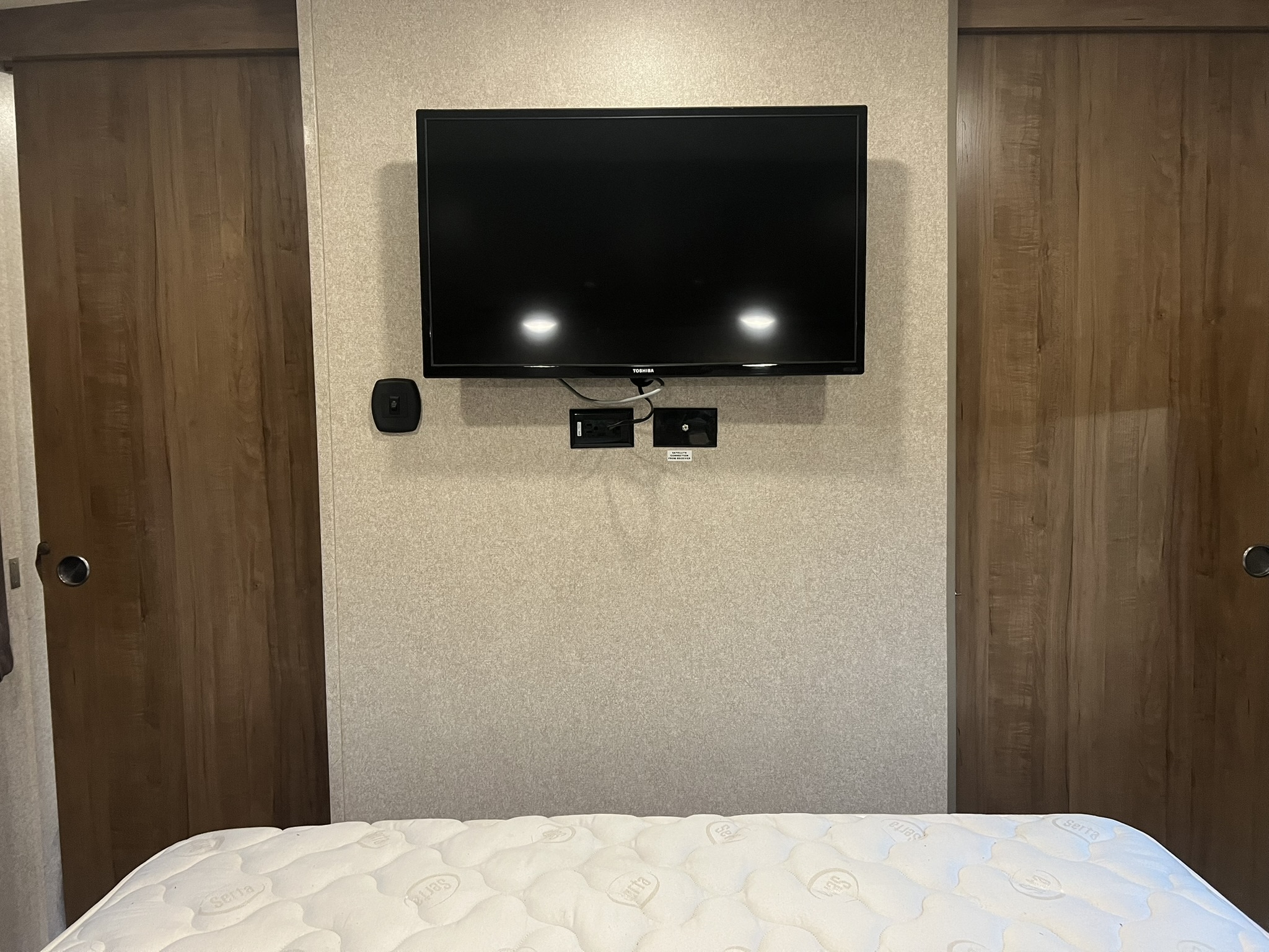 RV rental bedroom featuring a wall-mounted TV, Serta mattress, and wooden sliding doors on both sides.. Forest River Rockwood Signature Ultra Lite 2017