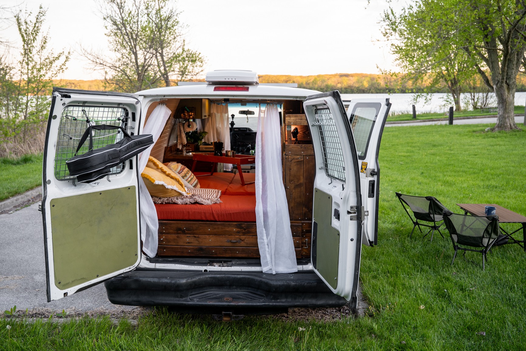 An RV rental's back doors are open, revealing a cozy van life interior with a bed, ready for a serene outdoor trip.. Ford Econoline 2012