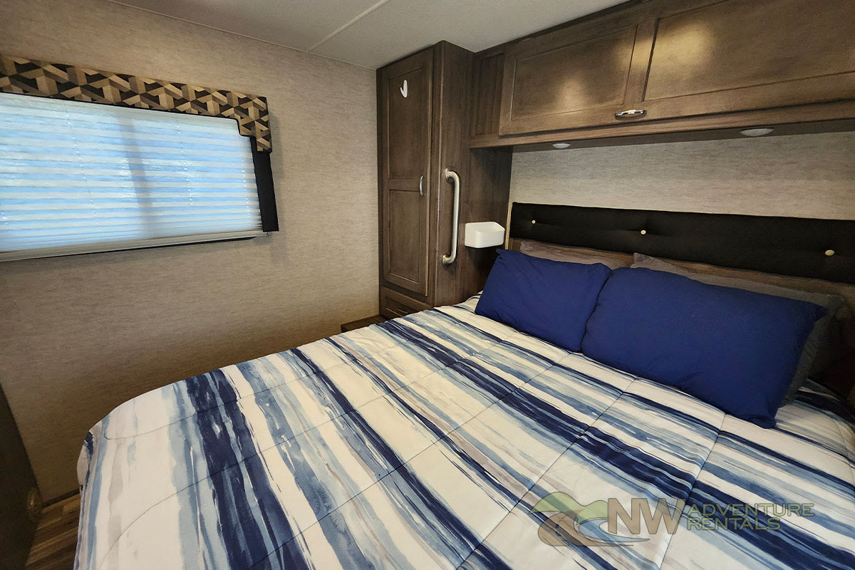 Inside an RV rental bedroom: a comfortable bed with blue & white striped bedding, blue pillows, and practical storage.. Winnebago Spirit 2018