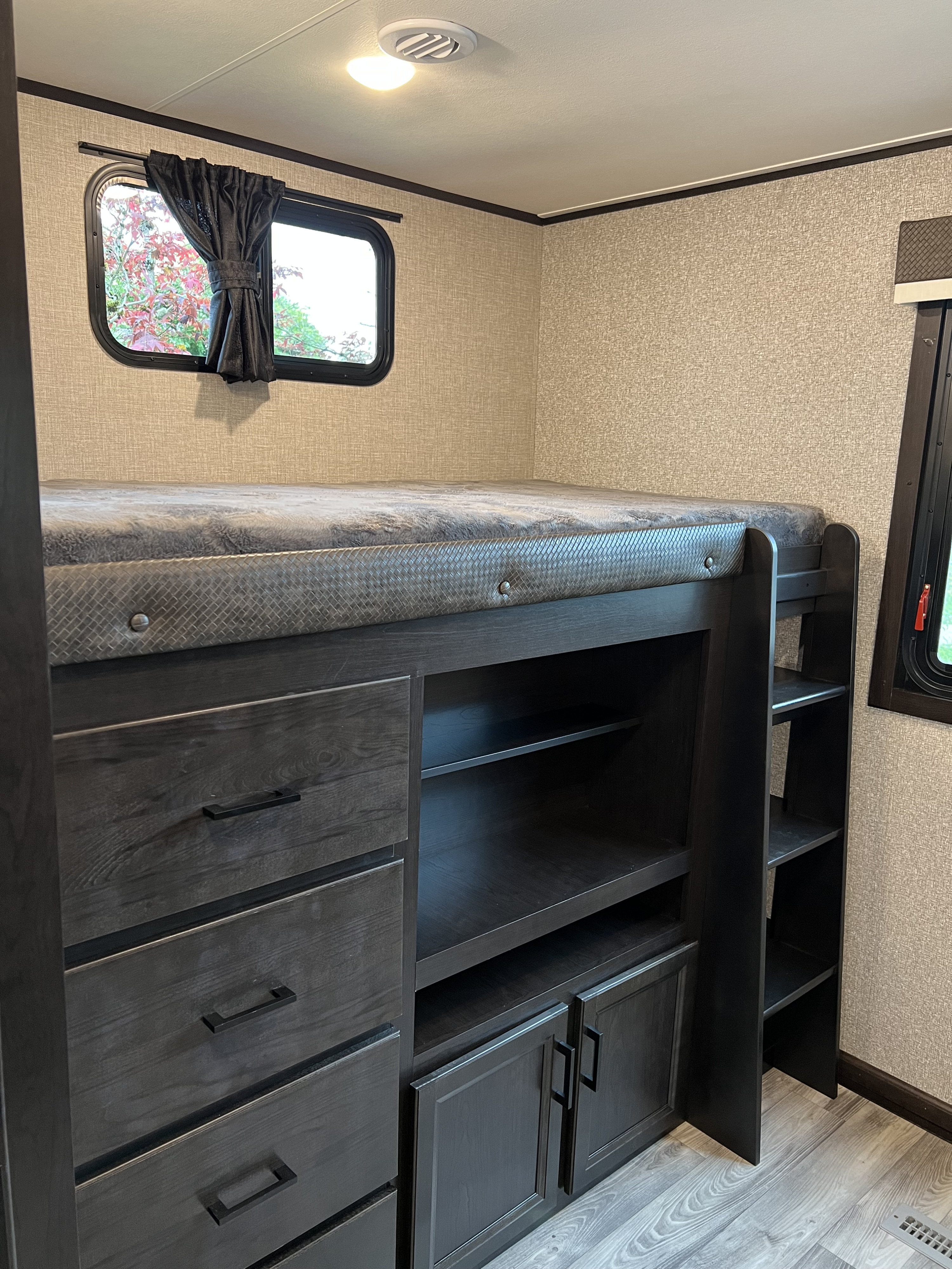 Cozy RV rental bedroom featuring a bunk bed with built-in dark wood drawers, shelves, and cabinets. Includes a window.. Jayco Eagle HT 2022