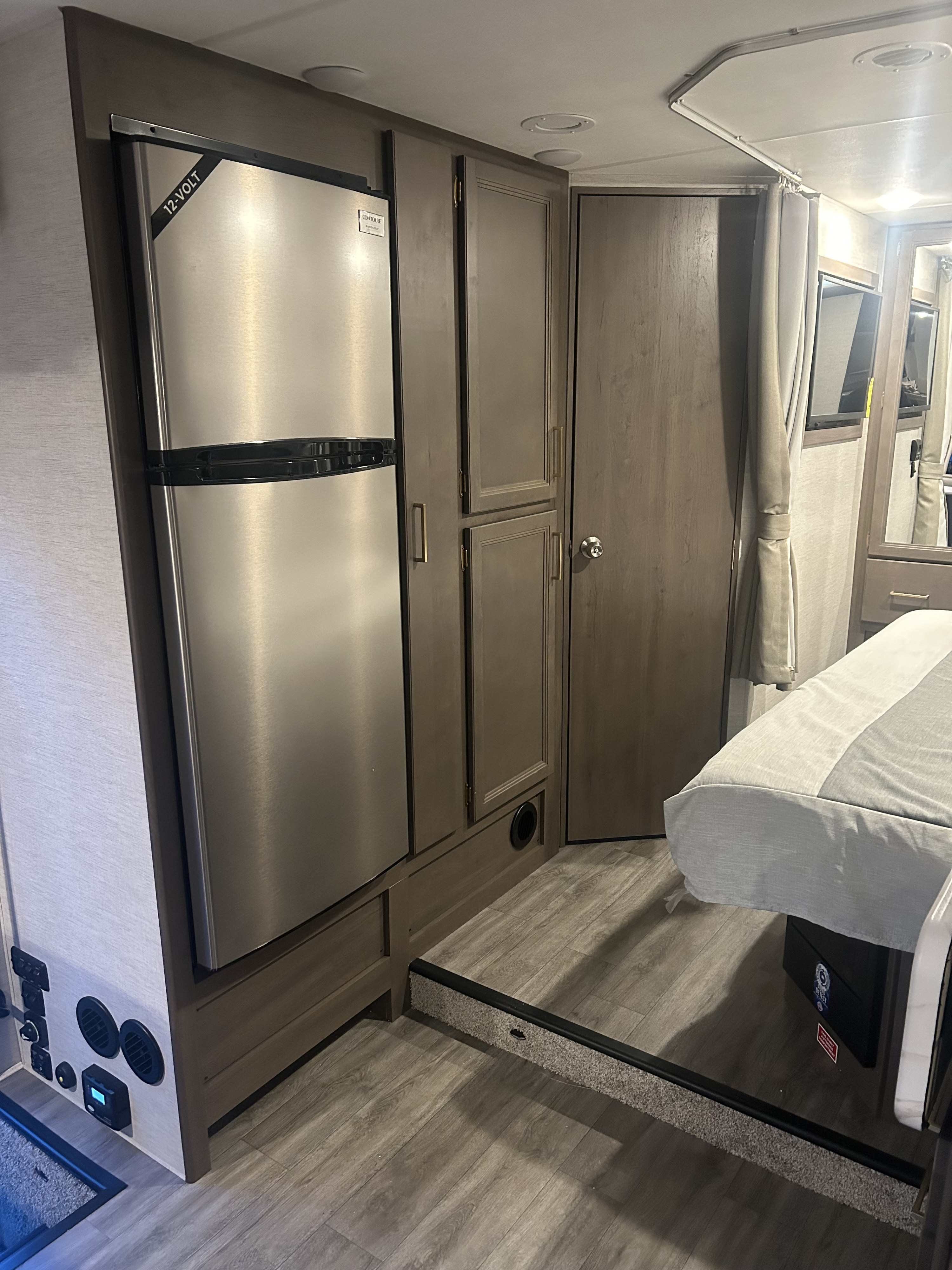 Modern RV rental interior with stainless 12-volt fridge, wood cabinets, and elevated bed. Compact living space.. Thor Four Winds 2024