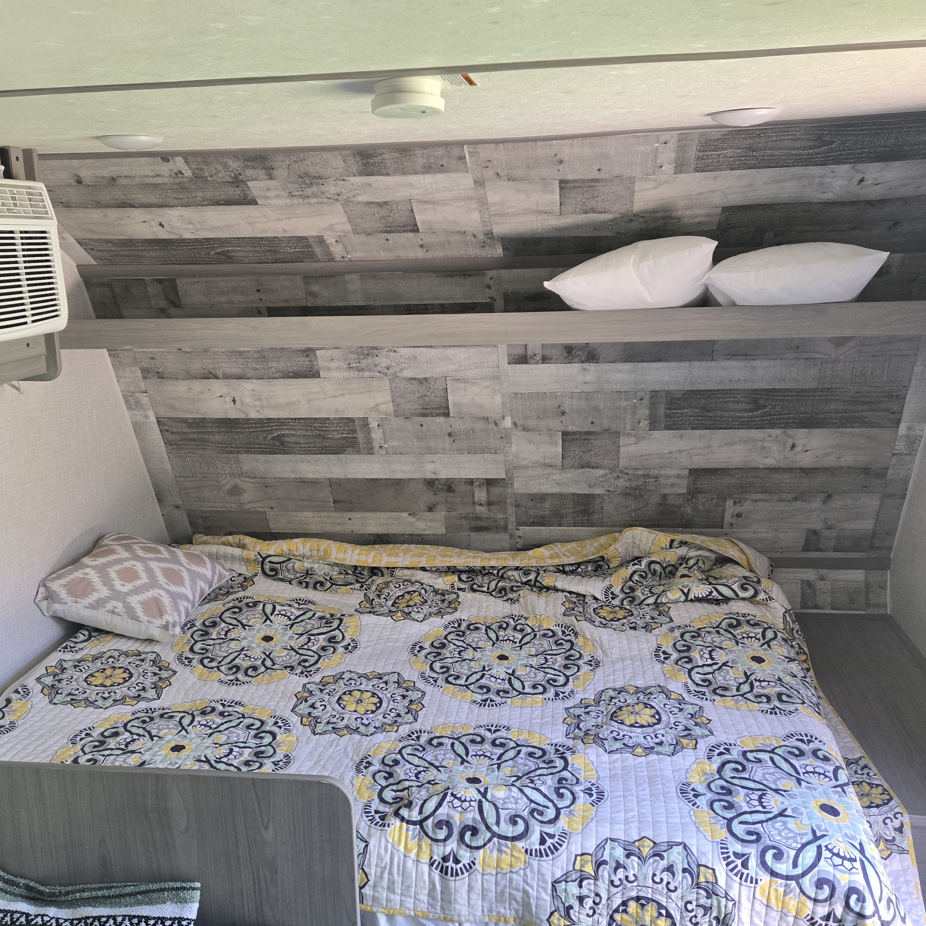 Cozy RV rental bedroom: patterned quilt, shelves with white pillows, and wood-look walls create an inviting, compact space.. Dutchmen Coleman Lantern LT 2023