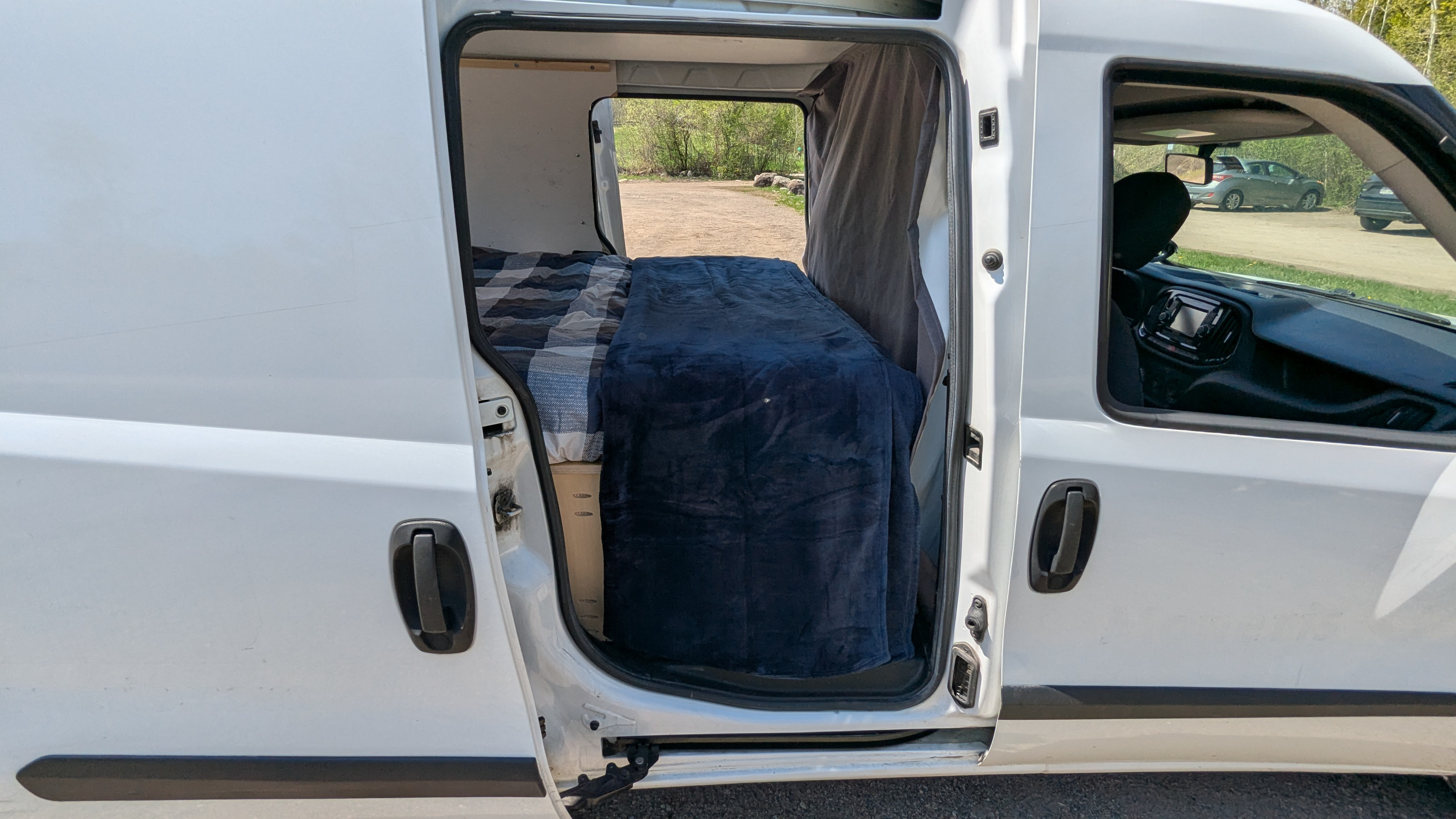 Explore comfort with this RV rental camper van. Side door open, revealing a cozy bed inside for your travels.. Dodge Promaster City 2015