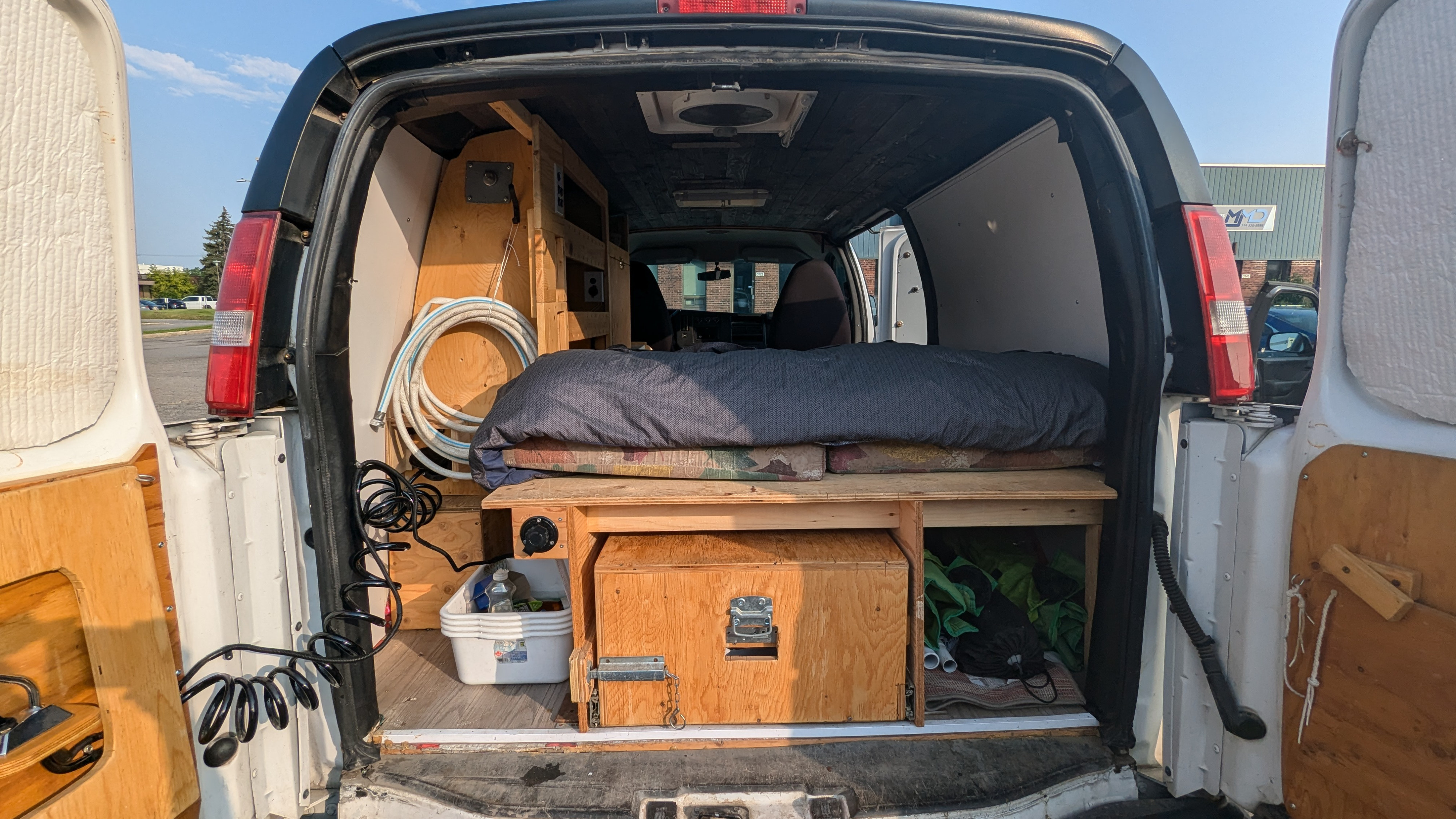 Inside an RV rental van conversion, showcasing the bed, custom storage, and utility setup for travel.. Gmc Savanna 2015