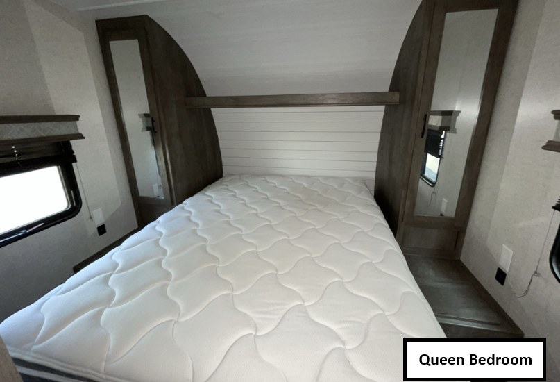 Cozy queen bedroom in an RV rental, featuring a comfortable bed, mirrored cabinets, and a window for natural light.. Forest River Shockwave 2021