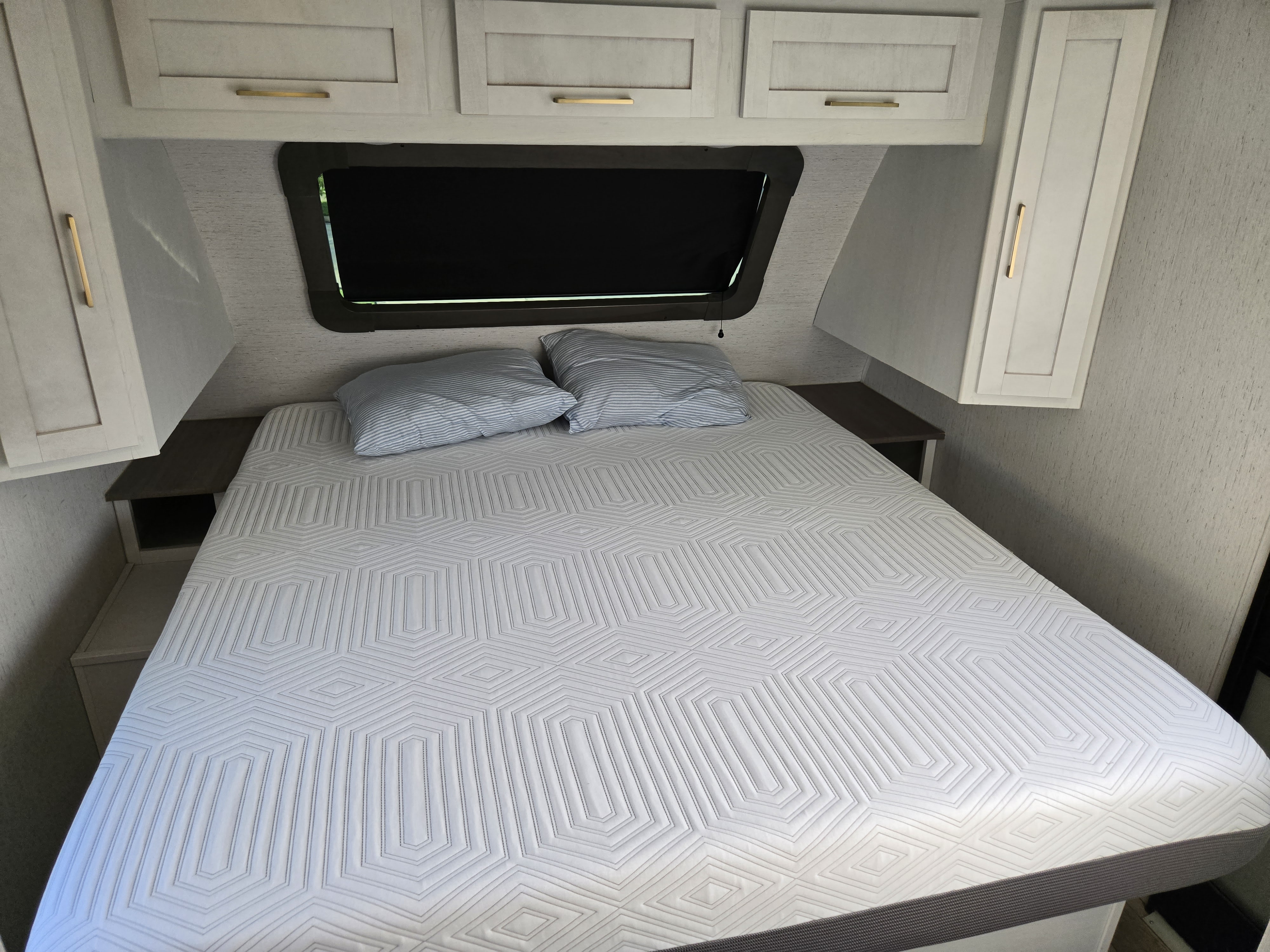 RV rental bedroom: Light-colored bed with geometric mattress, pillows, overhead cabinets, and window.. Dutchman Astroia 2022