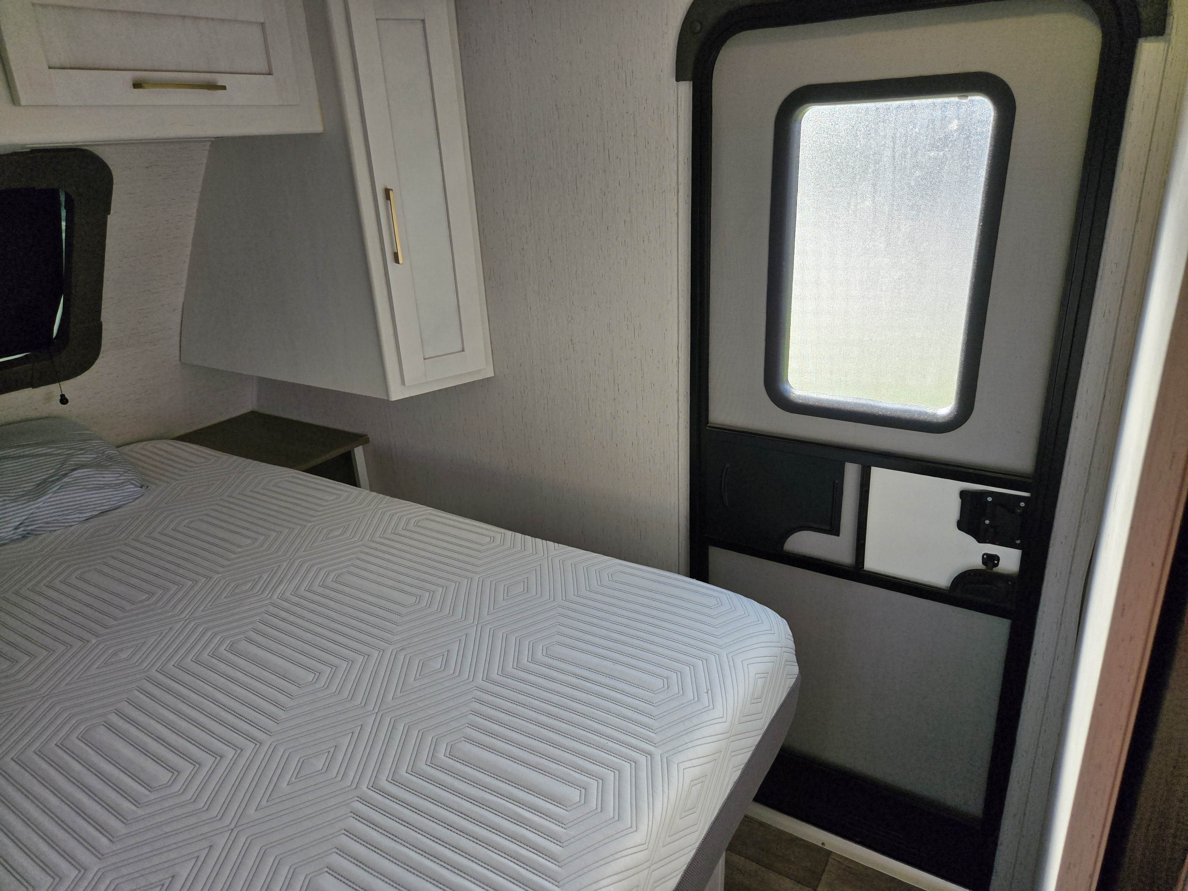 Cozy RV rental bedroom with patterned mattress, storage cabinet, and frosted door window for privacy.. Dutchman Astroia 2022