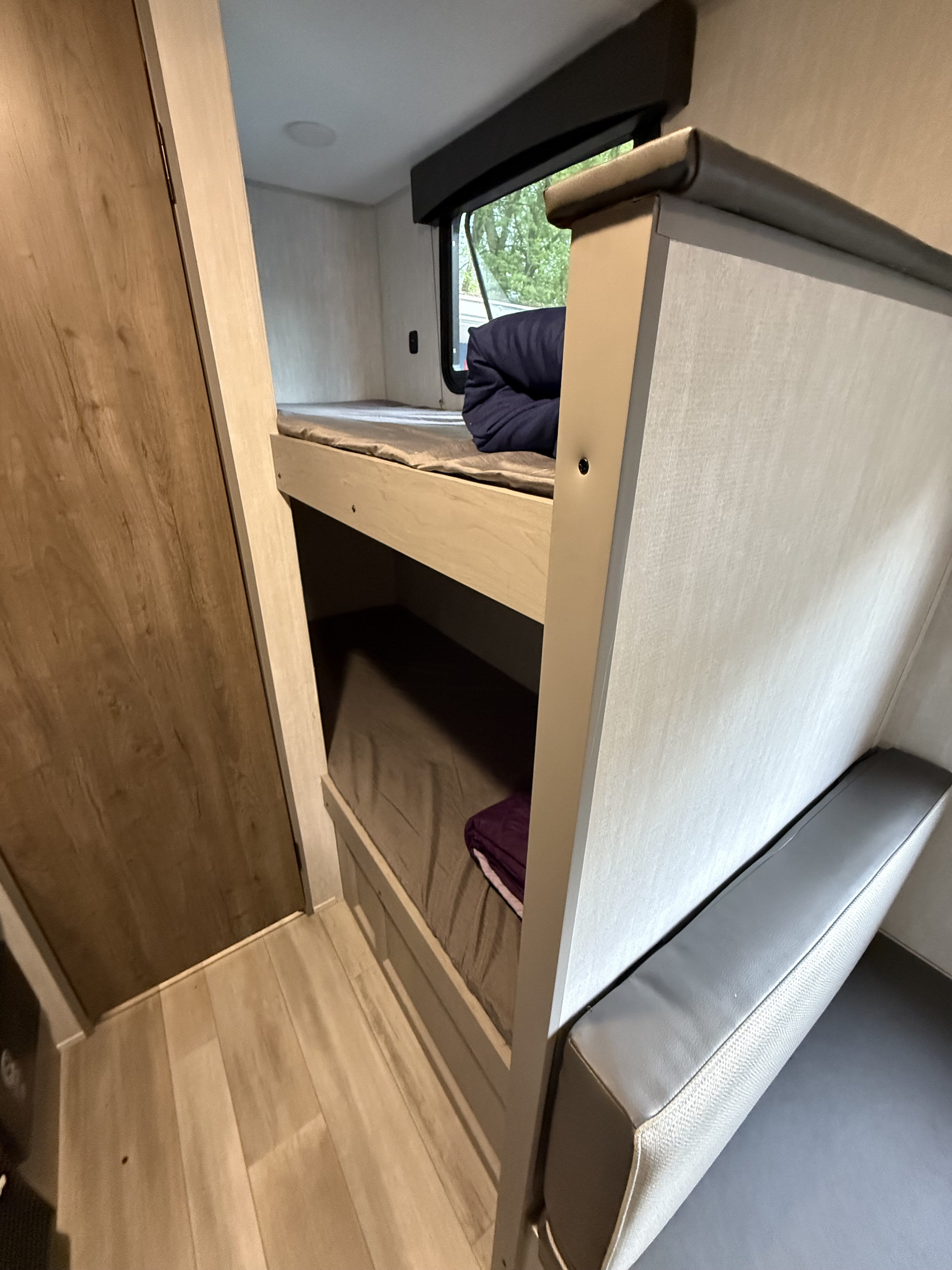 Inside an RV rental: upper and lower bunk beds with blankets, and a grey cushioned seating area, suitable for family trips.. Coachmen clipper cadet 17CBH 2025