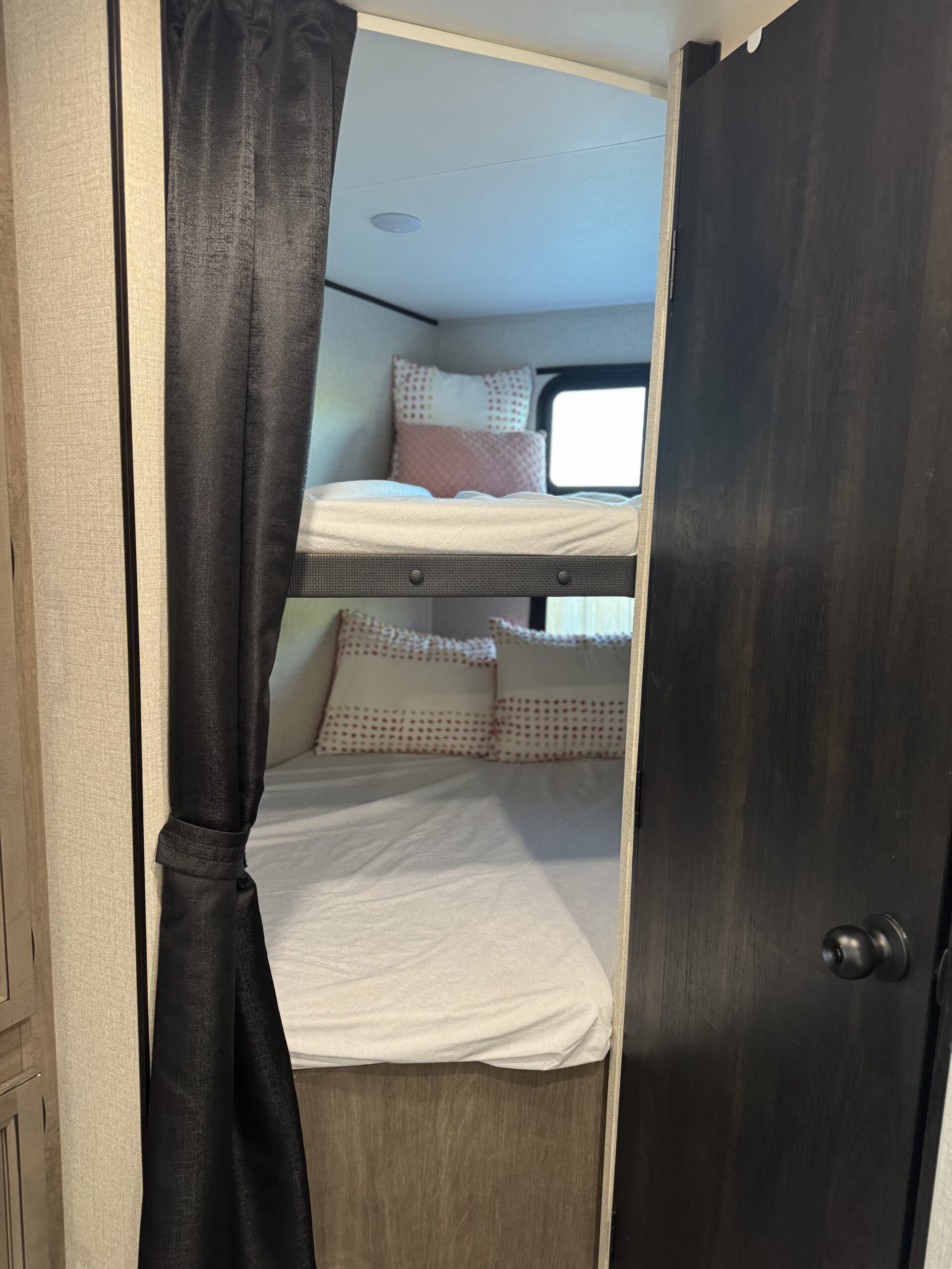 Cozy RV rental bunk beds with white sheets, pink pillows, and a privacy curtain, offering a comfortable sleeping area.. Starcraft Autumn Ridge 2022