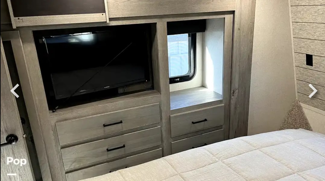 Cozy RV rental bedroom with a mounted TV, built-in storage drawers, and a bright window next to the bed.. Keystone RV Raptor Toy Hauler 2020