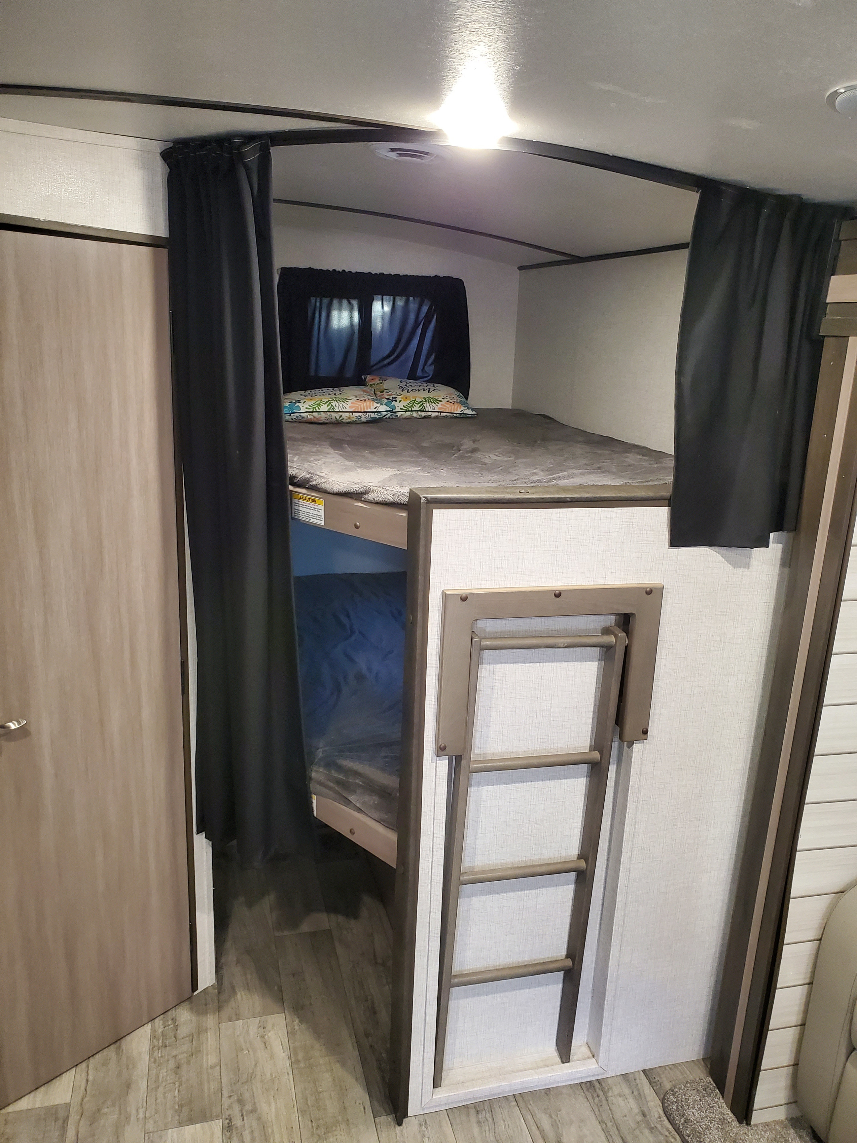 RV rental bunk beds: a cozy, compact sleeping area featuring privacy curtains, a ladder, and bedding.. Crossroads Sunset Trail Super Lite 2021