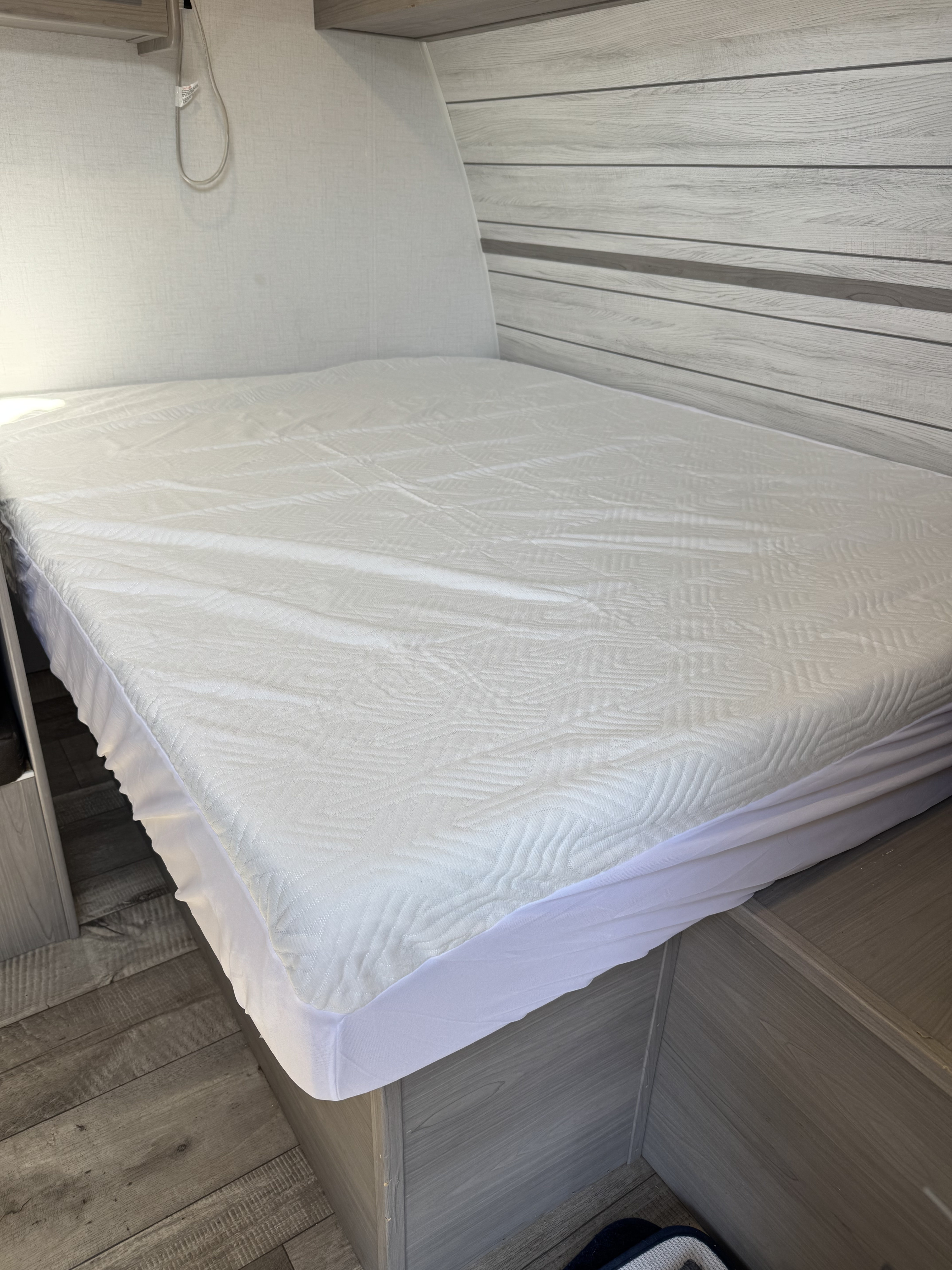RV rental bed: White mattress cover on a modern bed with light wood interior paneling.. Dutchmen Coleman 17B 2024