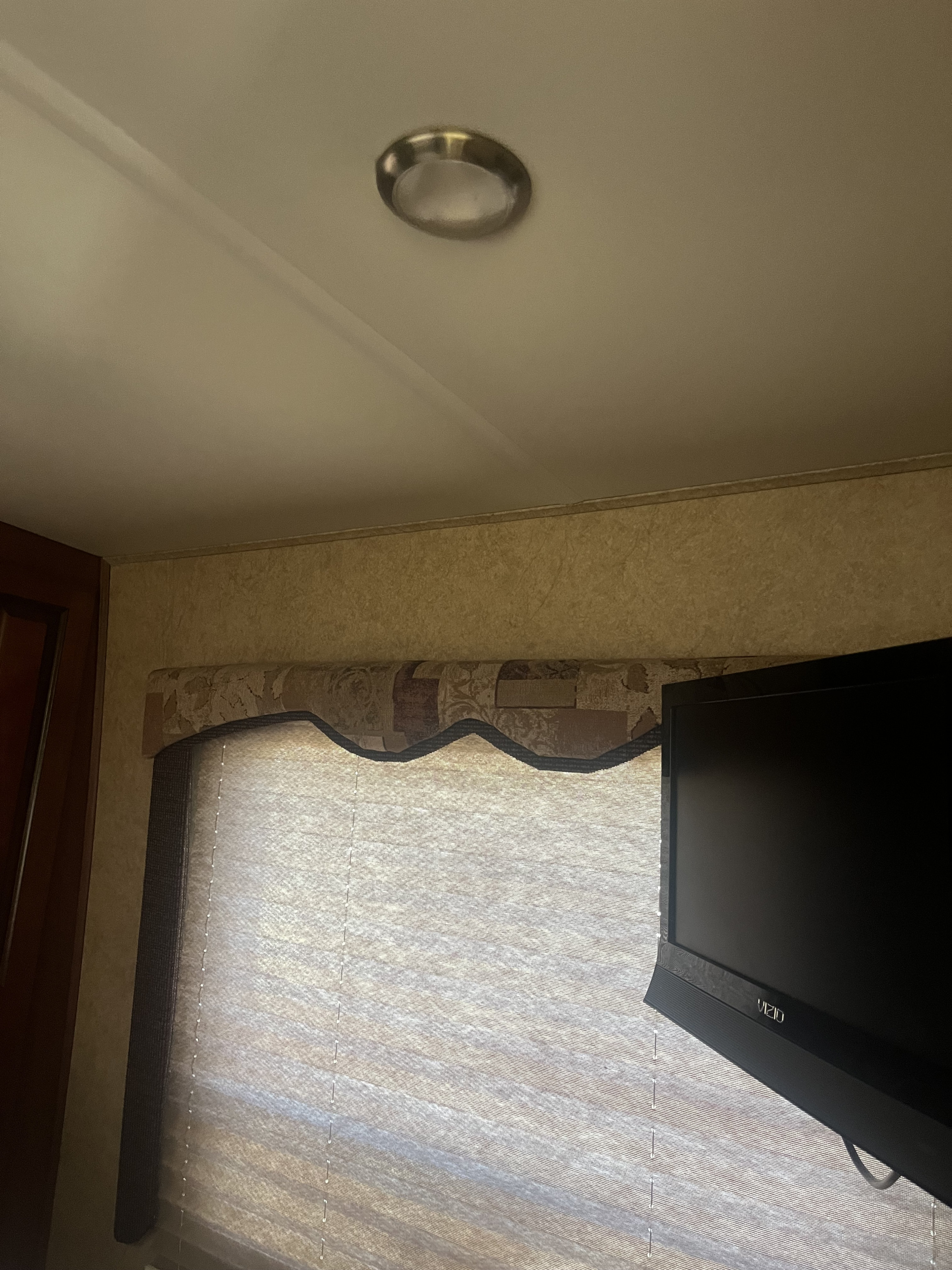 RV rental interior detail: overhead light, patterned wall, window with a blind and valance, plus a VIZIO TV.. Lexington Grand Touring 2010