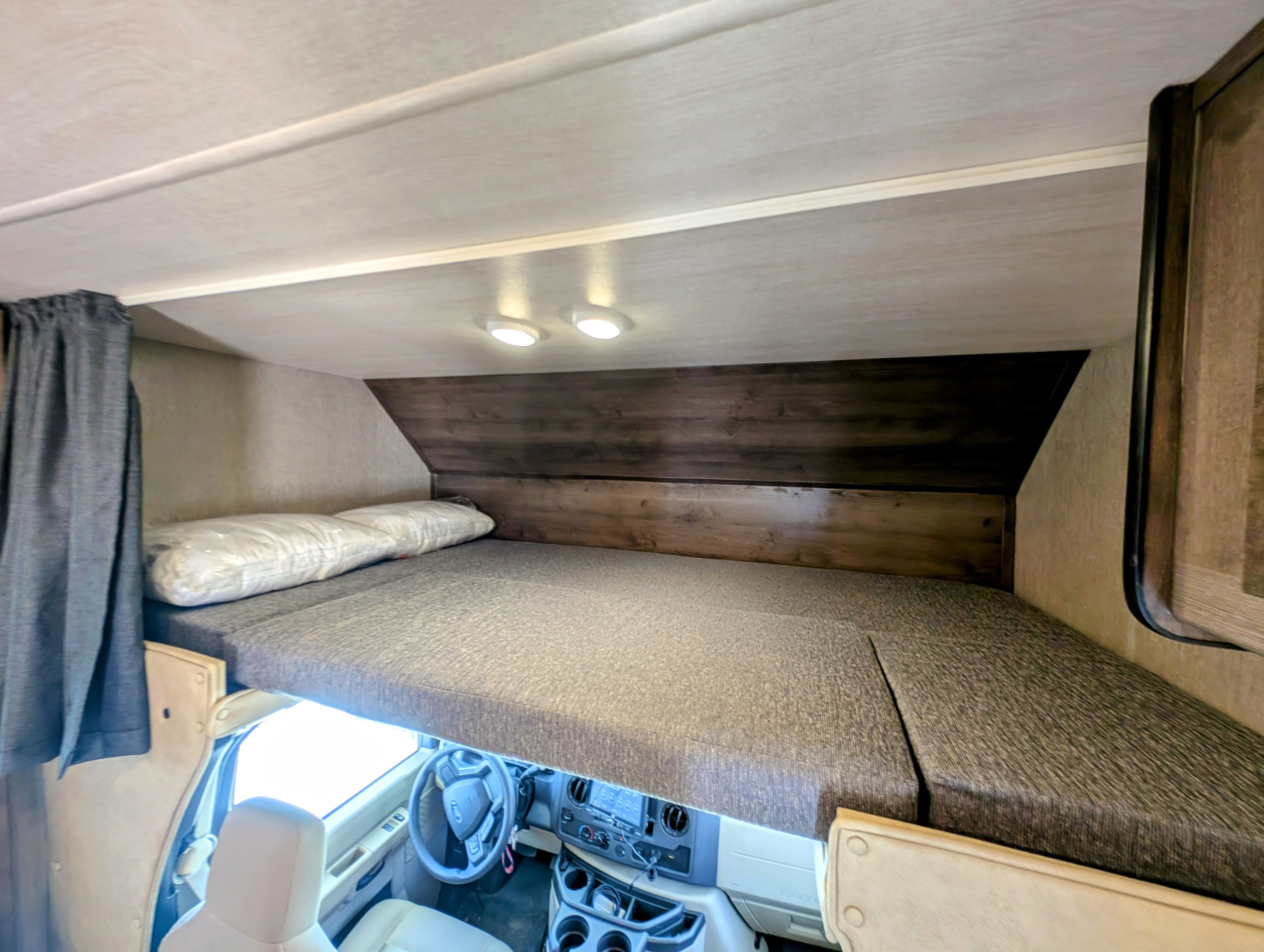 RV rental interior showing a cozy cab-over bunk with bedding, above the driver's cockpit.. Nexus RV Triumph 2023