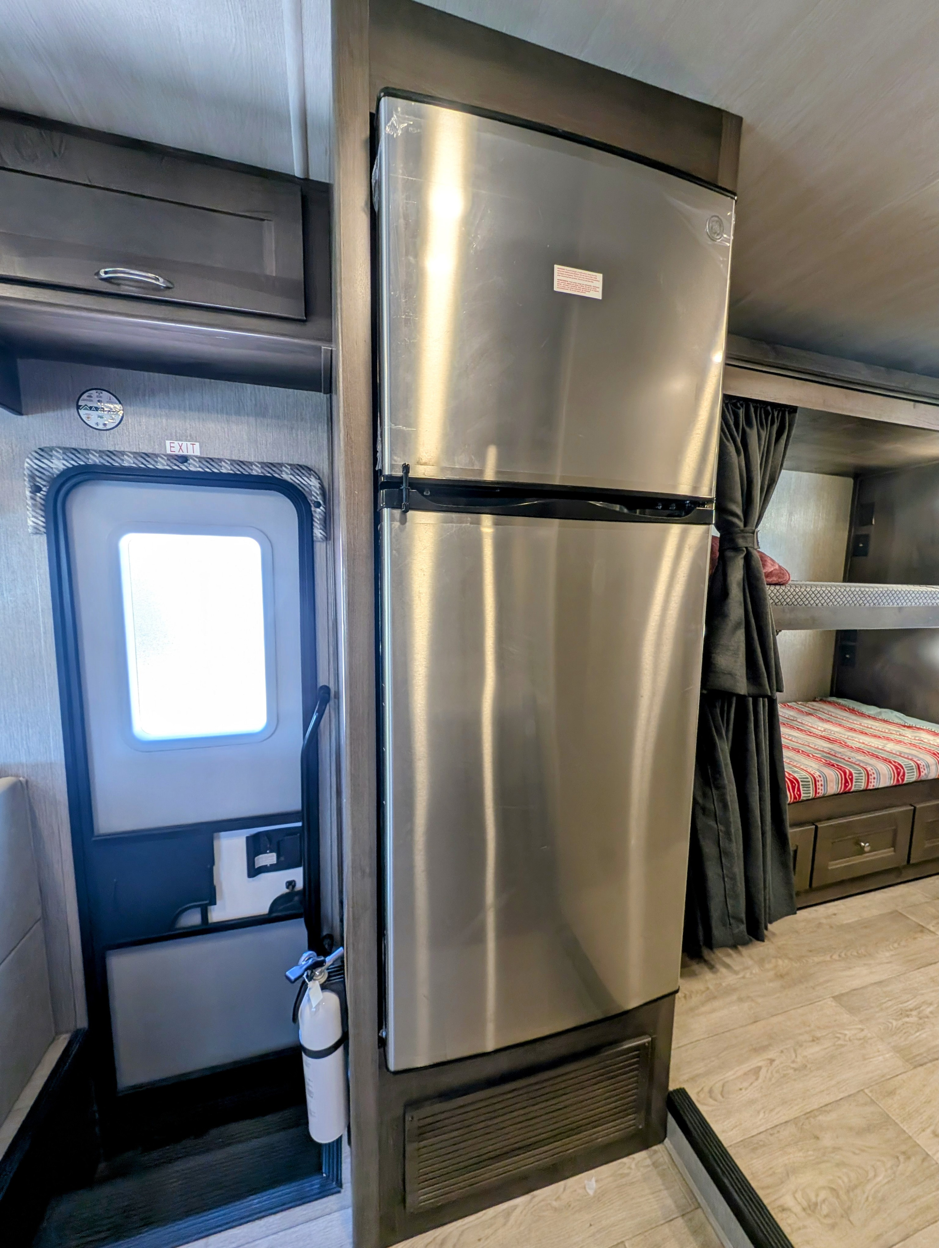 RV rental interior with stainless steel fridge, exit door, and bunk beds. Includes a fire extinguisher.. Nexus RV Triumph 2023