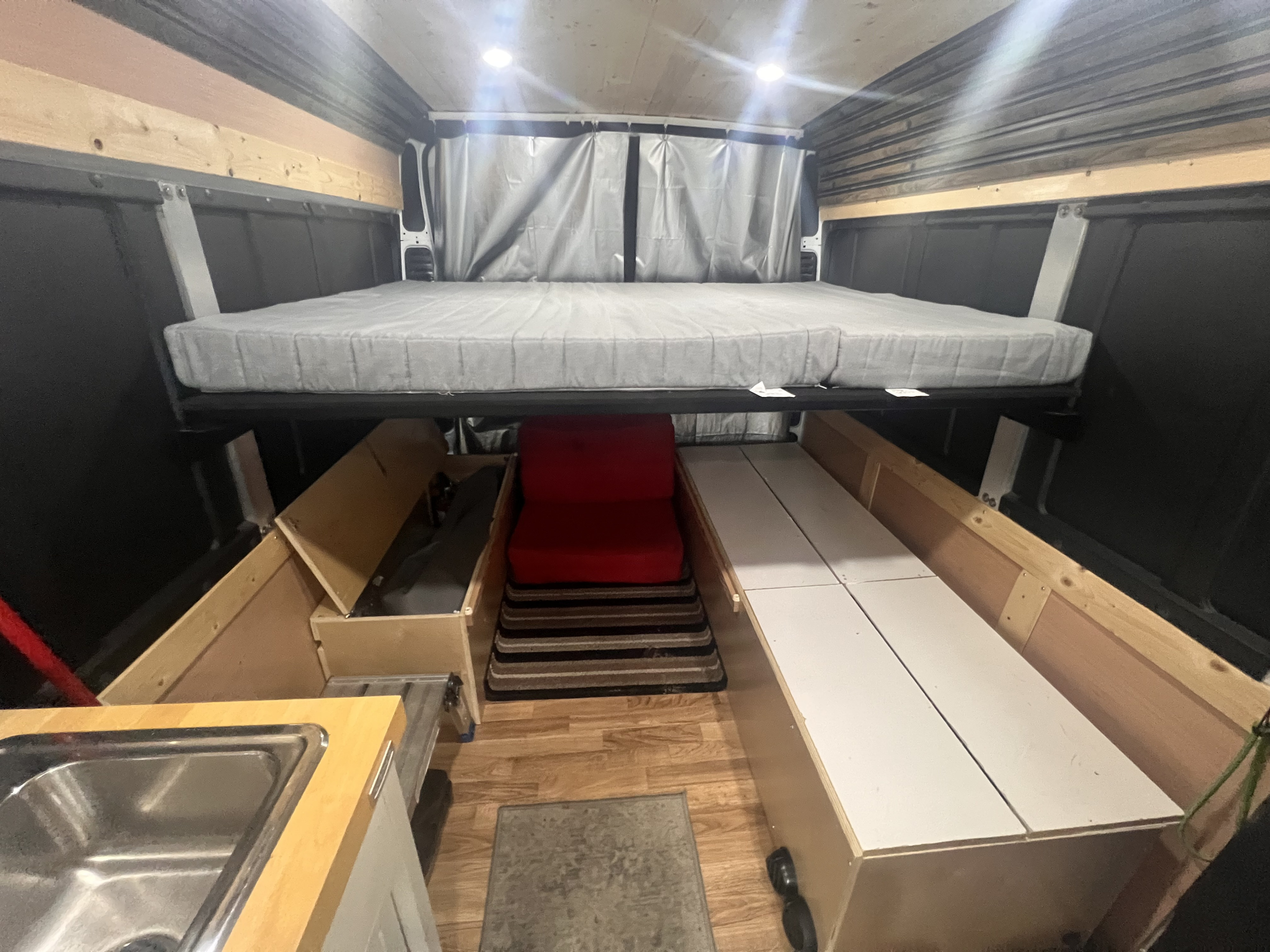 Spacious RV rental interior featuring a raised bed, sink, storage, and a cozy red chair, designed for travel comfort.. Ram Promaster 2019