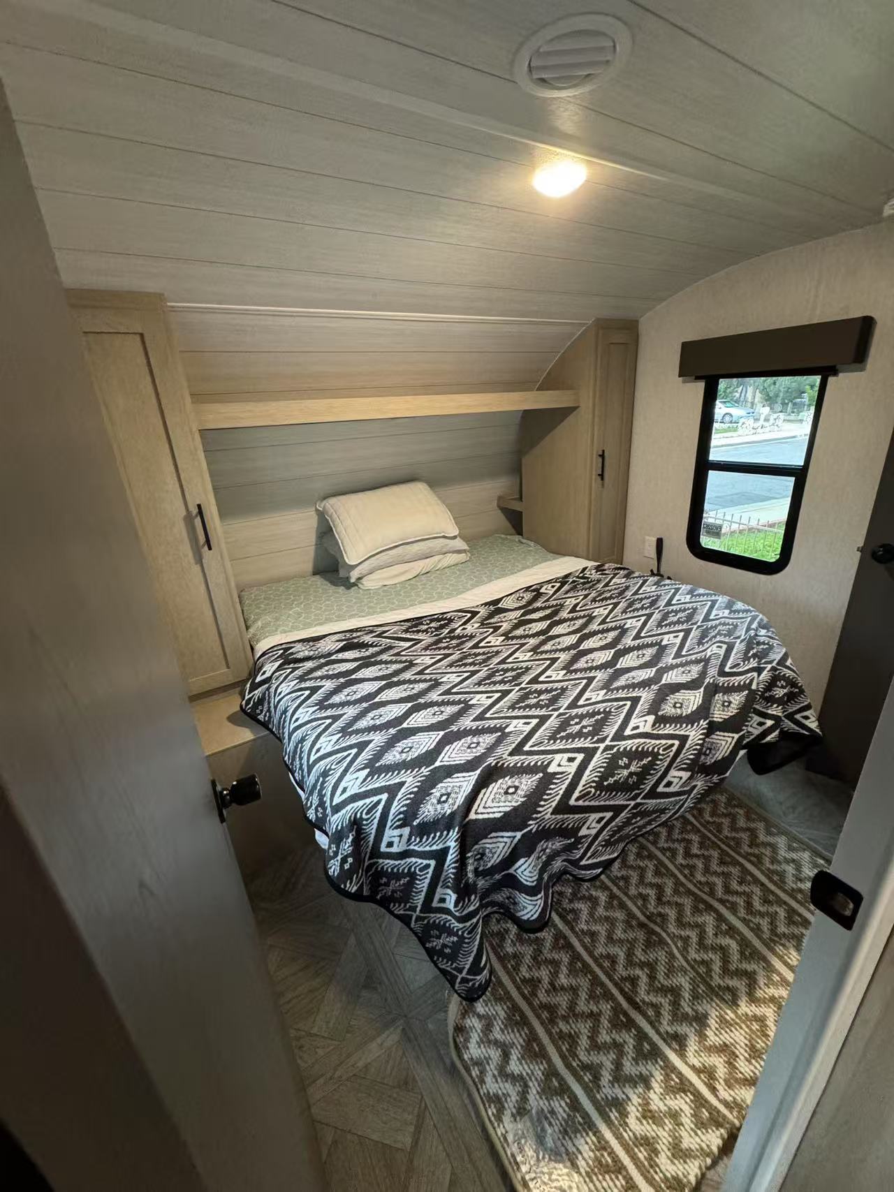 This RV rental bedroom features a comfy bed with a patterned blanket, built-in storage, and a window offering an outdoor view.. Forest River EVO 2024