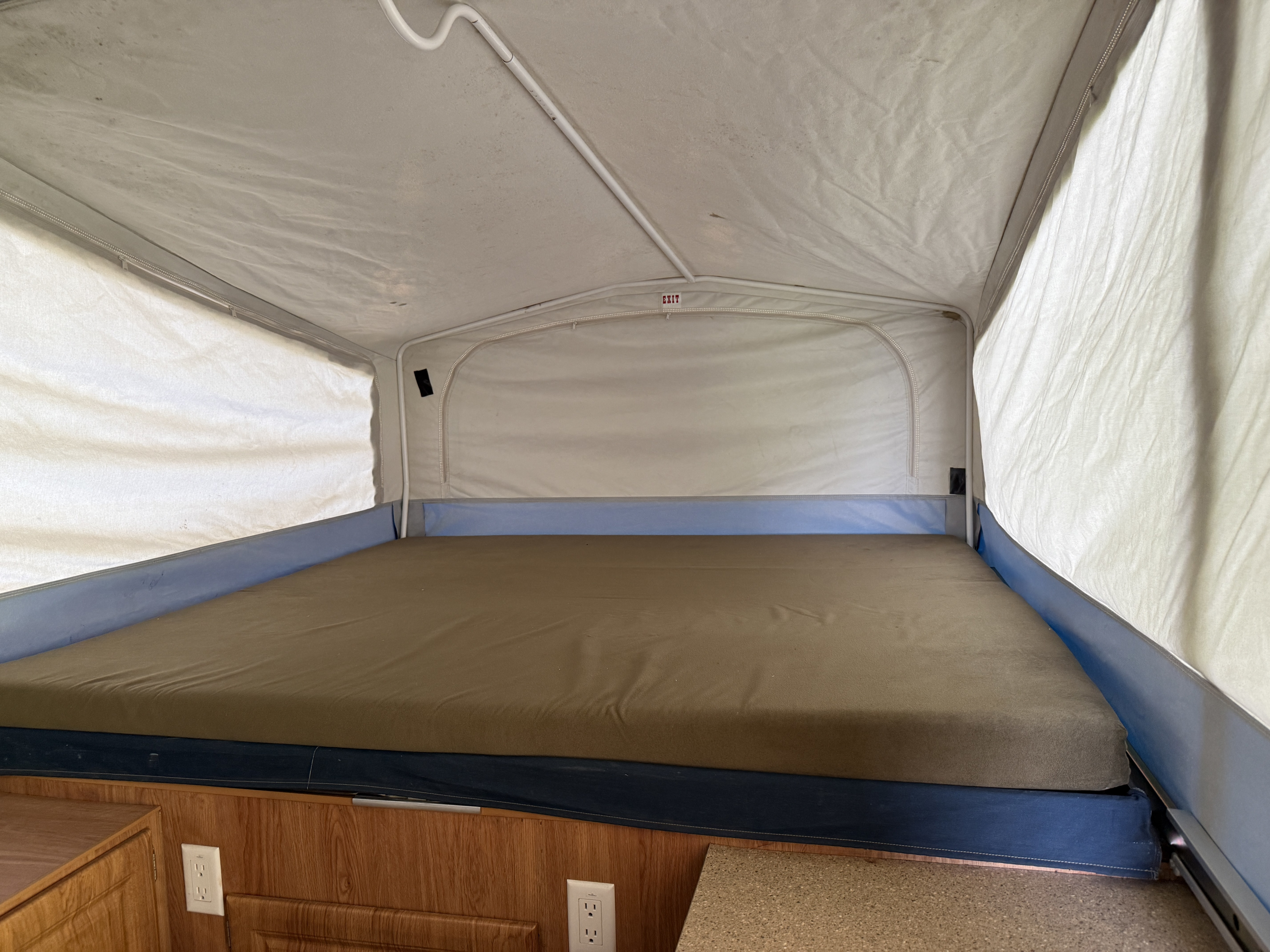 RV rental pop-up camper interior. View of the large bed with brown mattress & fabric walls, an 'EXIT' sign is visible.. Jayco Jay 2007
