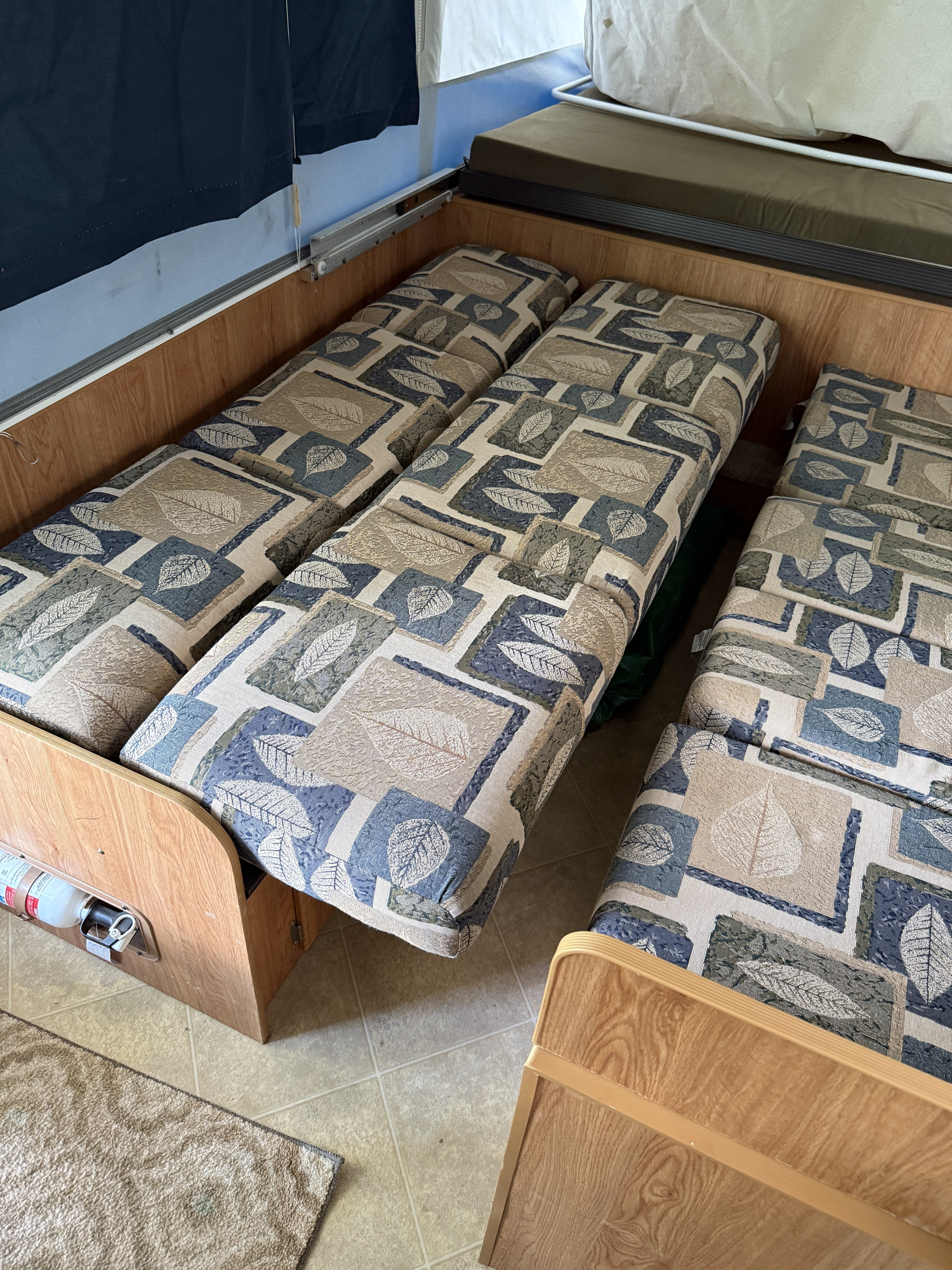 RV rental interior: patterned cushions forming a bed or seating area, with a fire extinguisher mounted on wood paneling.. Jayco Jay 2007
