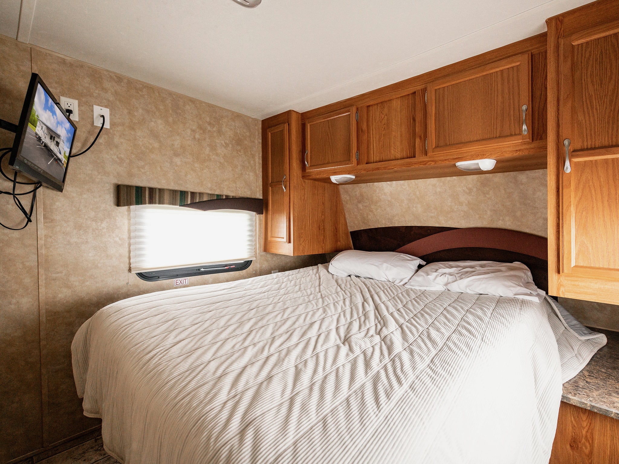 RV rental bedroom with a white bed, wooden cabinets, TV, and an emergency exit window for a comfortable stay.. Jayco Jay Flight 2010