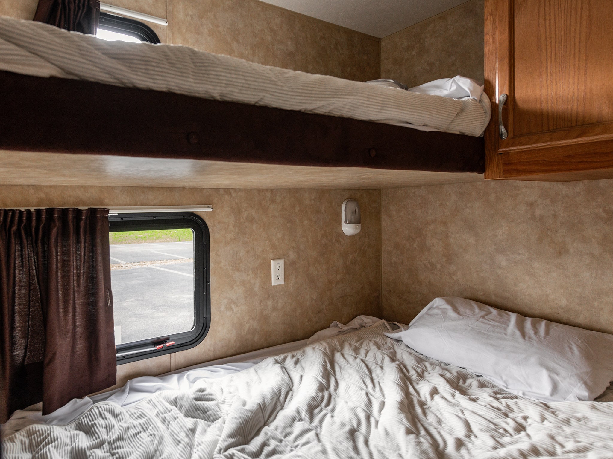 Inside an RV rental: clean bunk beds, one with striped bedding, the other with ribbed white. Window, outlet, and cabinet detail.. Jayco Jay Flight 2010
