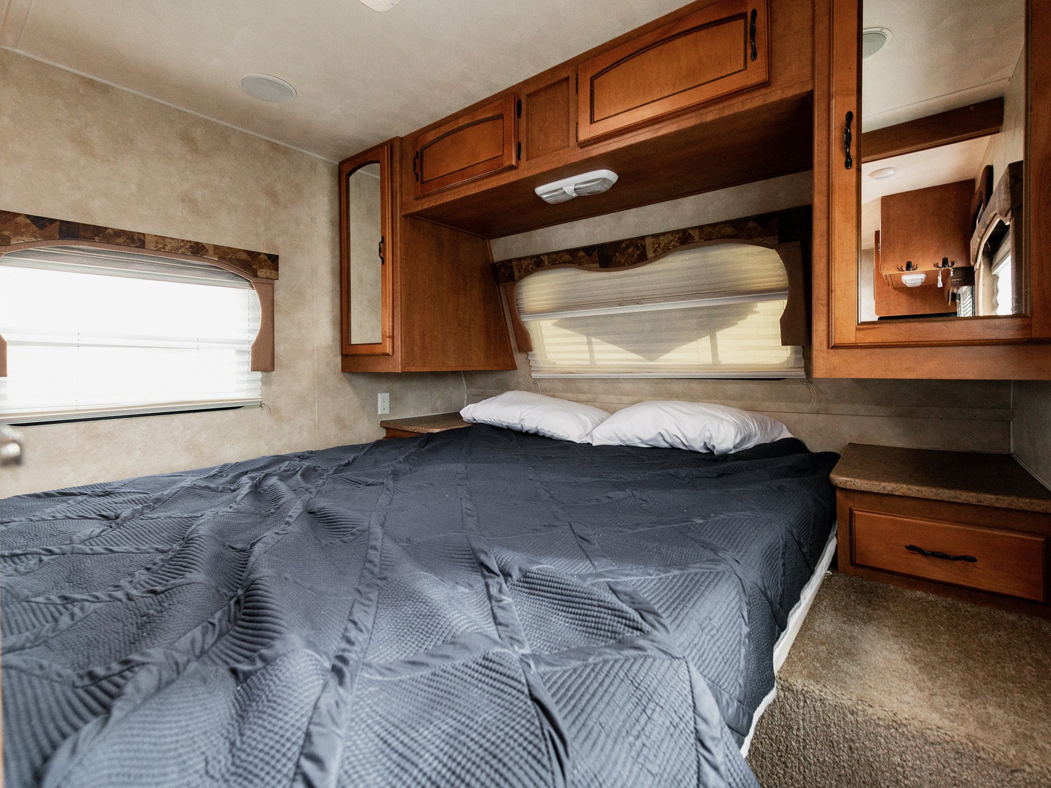 Inside a compact RV rental bedroom, featuring a large bed with a dark comforter, wooden cabinets, and windows.. Forest River Palomino Puma 2012