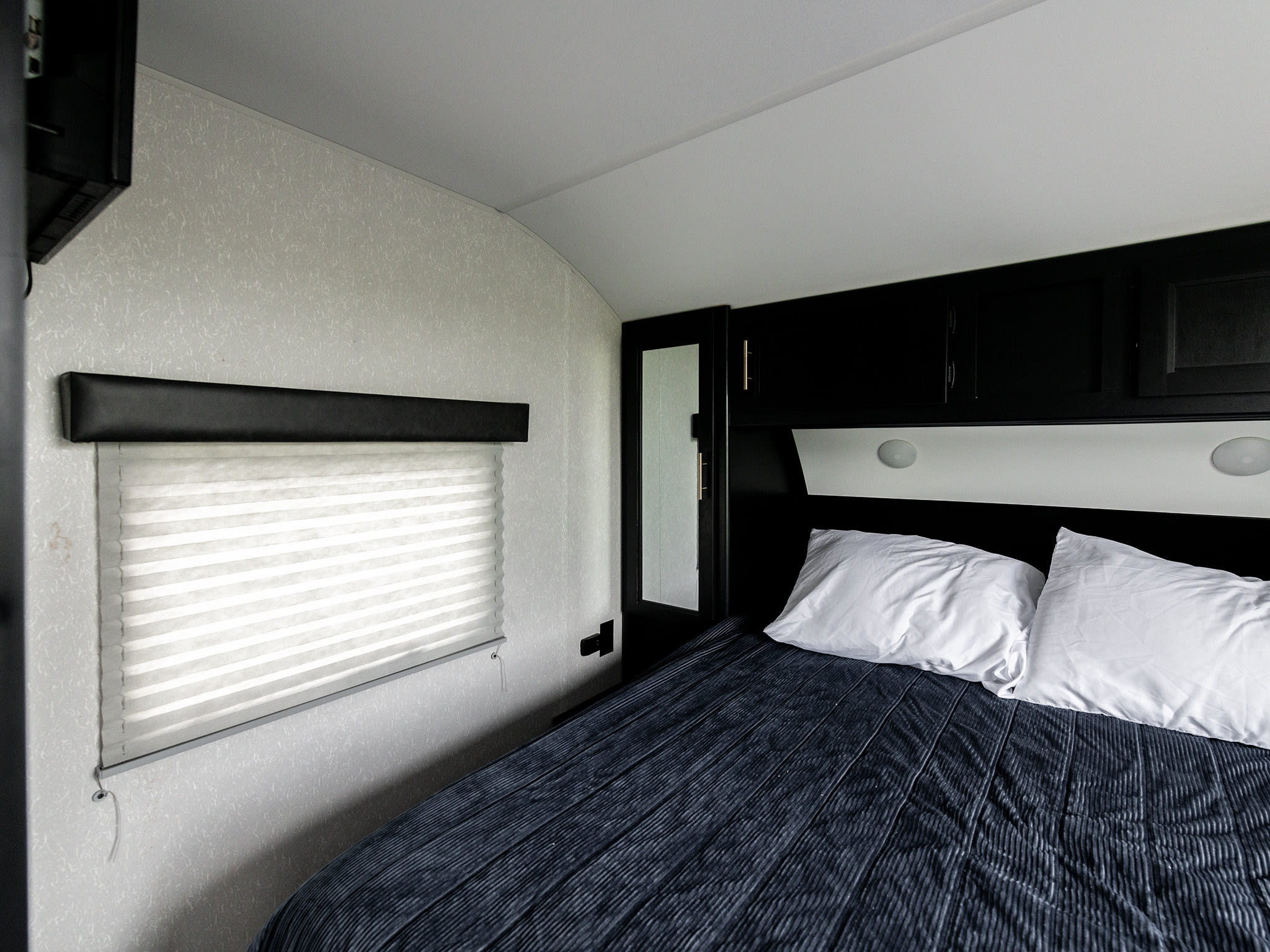 Cozy RV rental bedroom with dark blue bed, white pillows, window blinds, and black cabinets.. Forest River Cherokee Grey Wolf 2021