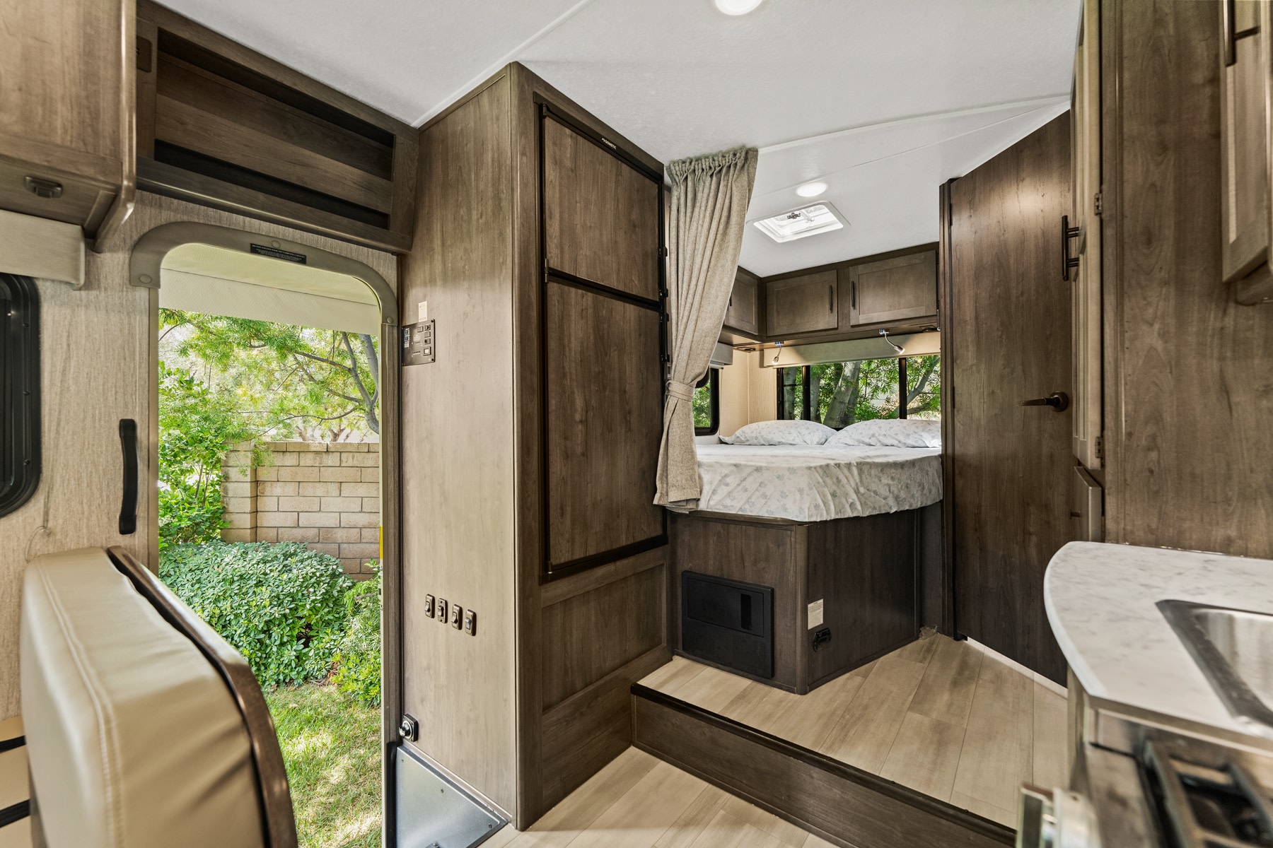 Cozy RV rental interior with a bed, kitchen counter, and exit door to a grassy yard, offering compact travel living.. COACHMEN Leprechaun 2023
