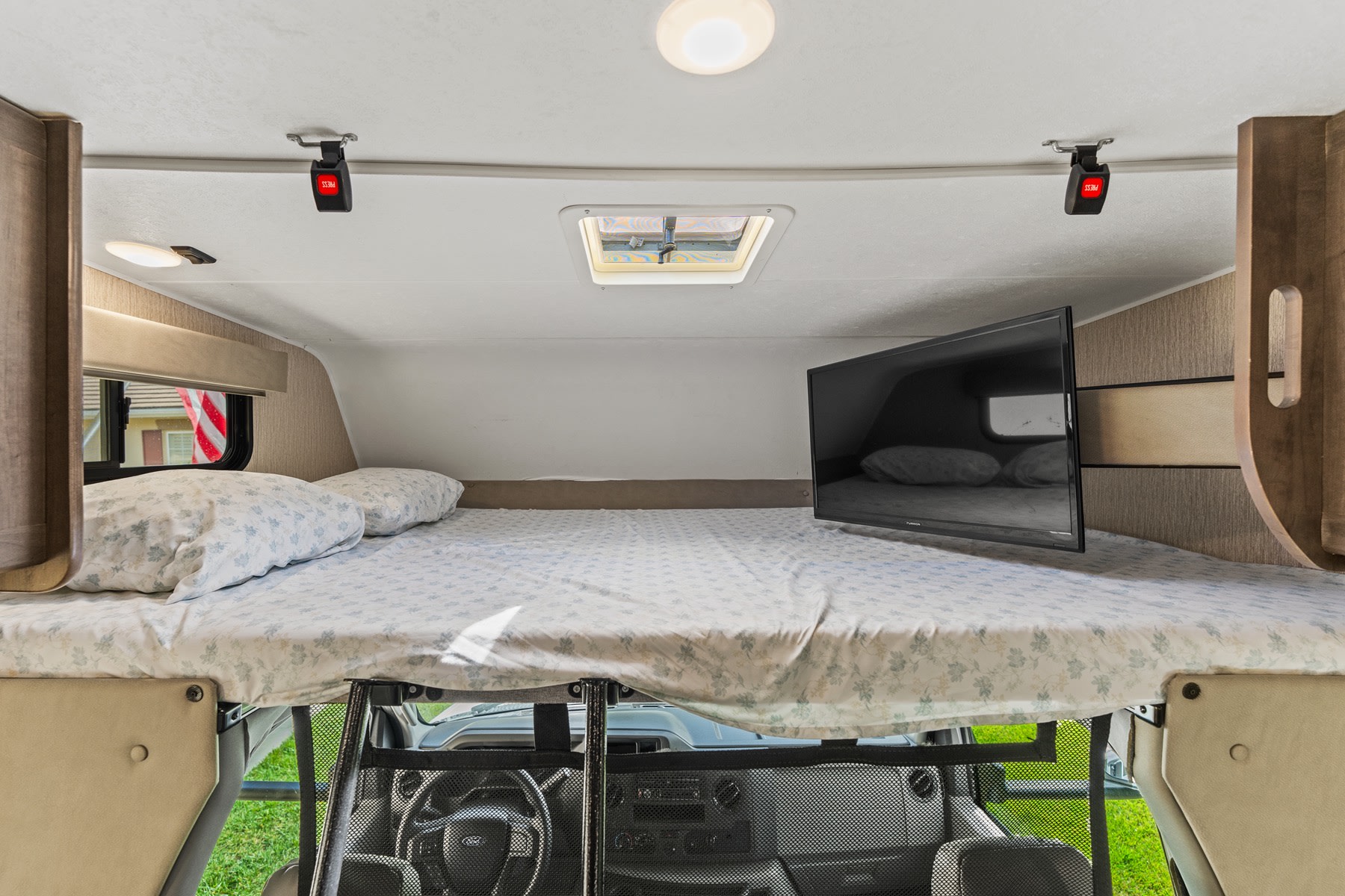 This RV rental's cab-over bunk offers a cozy sleeping area with a comfortable bed, TV, and skylight.. COACHMEN Leprechaun 2023