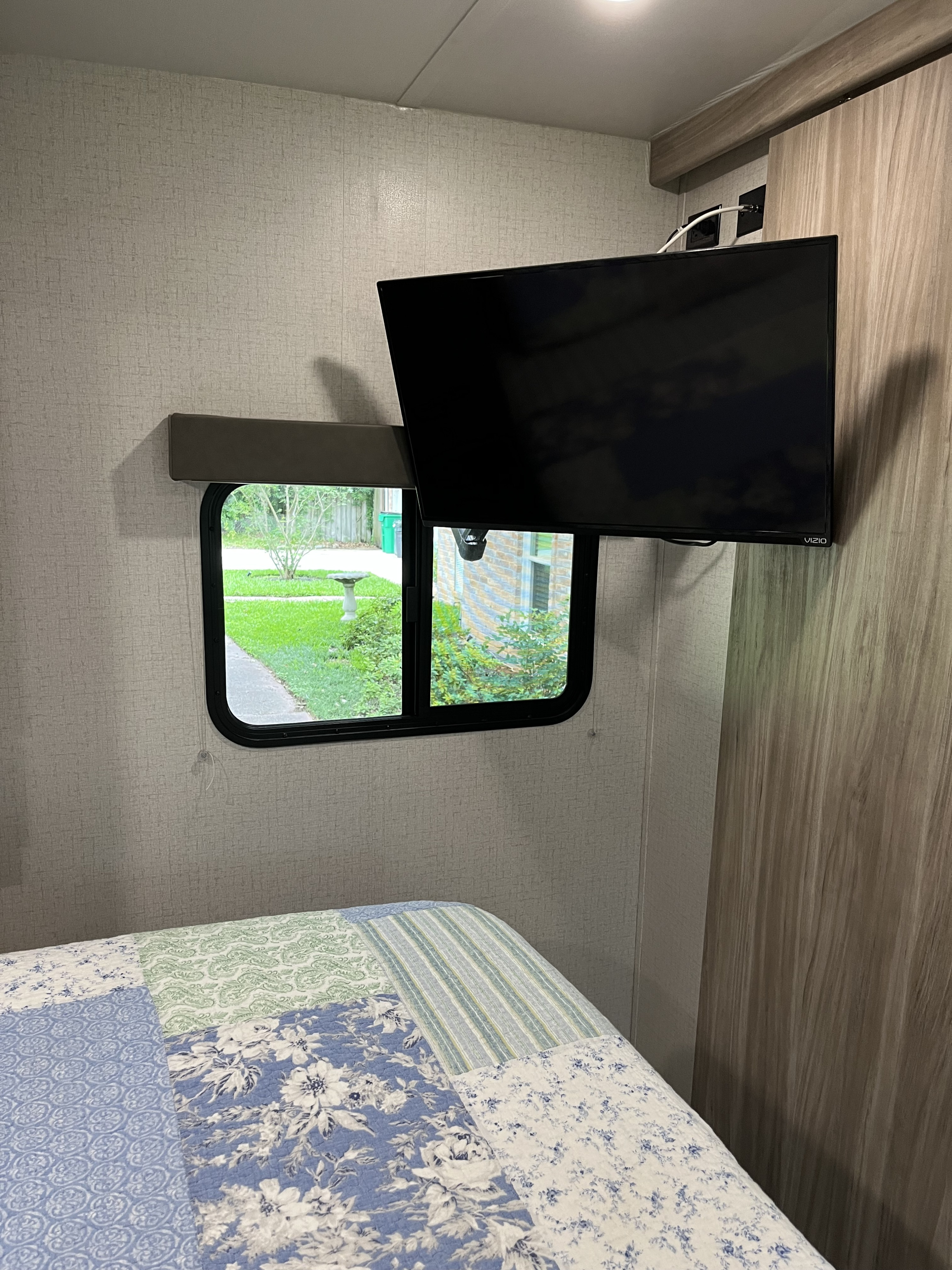 RV rental bedroom: a bed with a patchwork quilt, window overlooking a green yard, and a wall-mounted Vizio TV.. Winnebago Minnie Winnie 2022