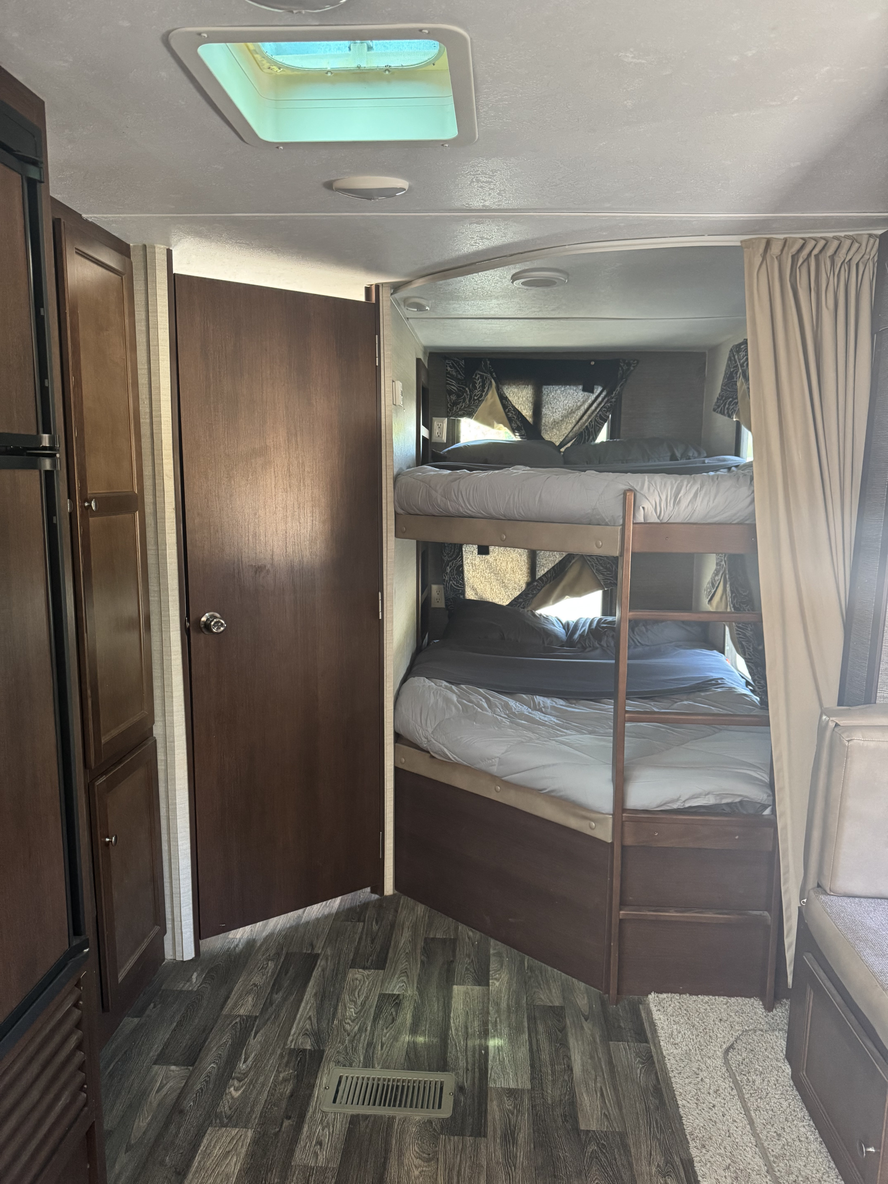 RV rental interior featuring bunk beds with a ladder, dark wood cabinets, a refrigerator unit, and wood-look flooring.. Keystone RV Bullet Ultra Lite 2017