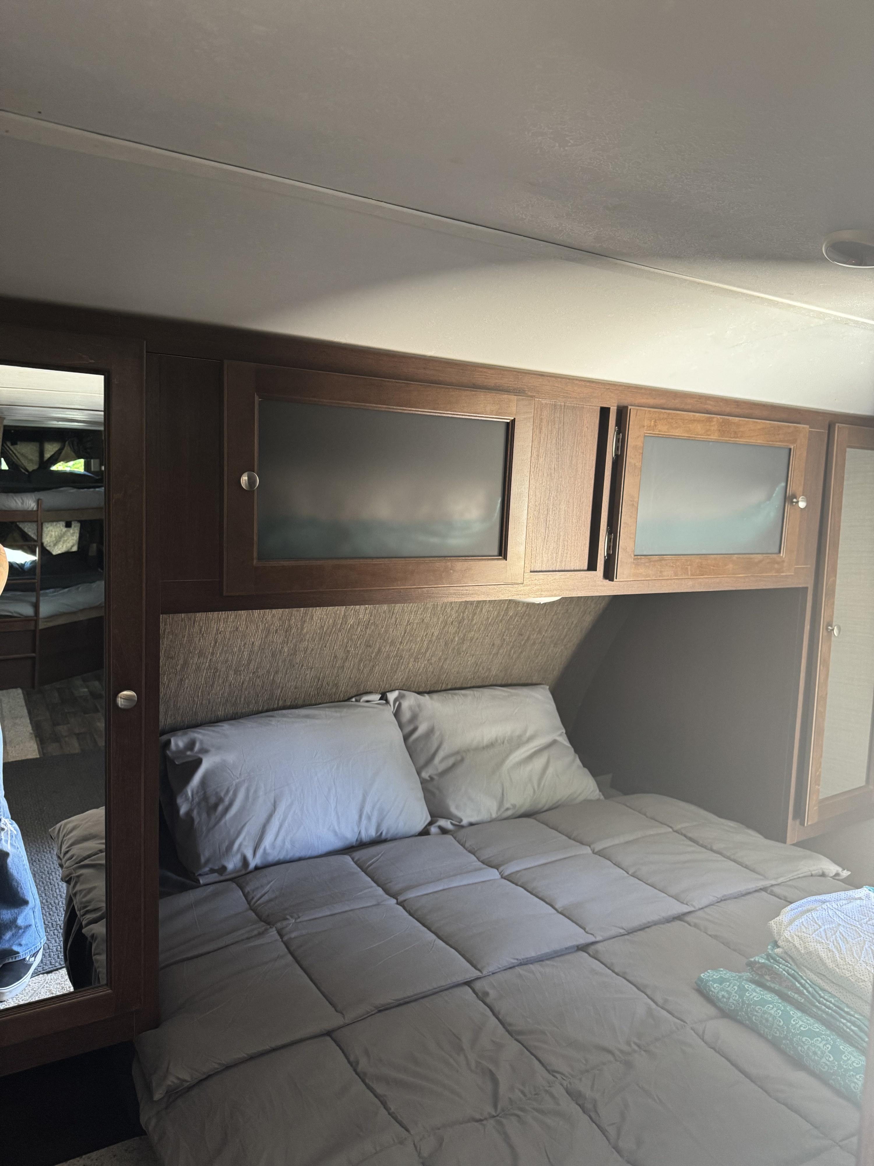 Cozy RV rental bedroom with a gray bed, overhead cabinets, and a mirror reflecting bunk beds.. Keystone RV Bullet Ultra Lite 2017