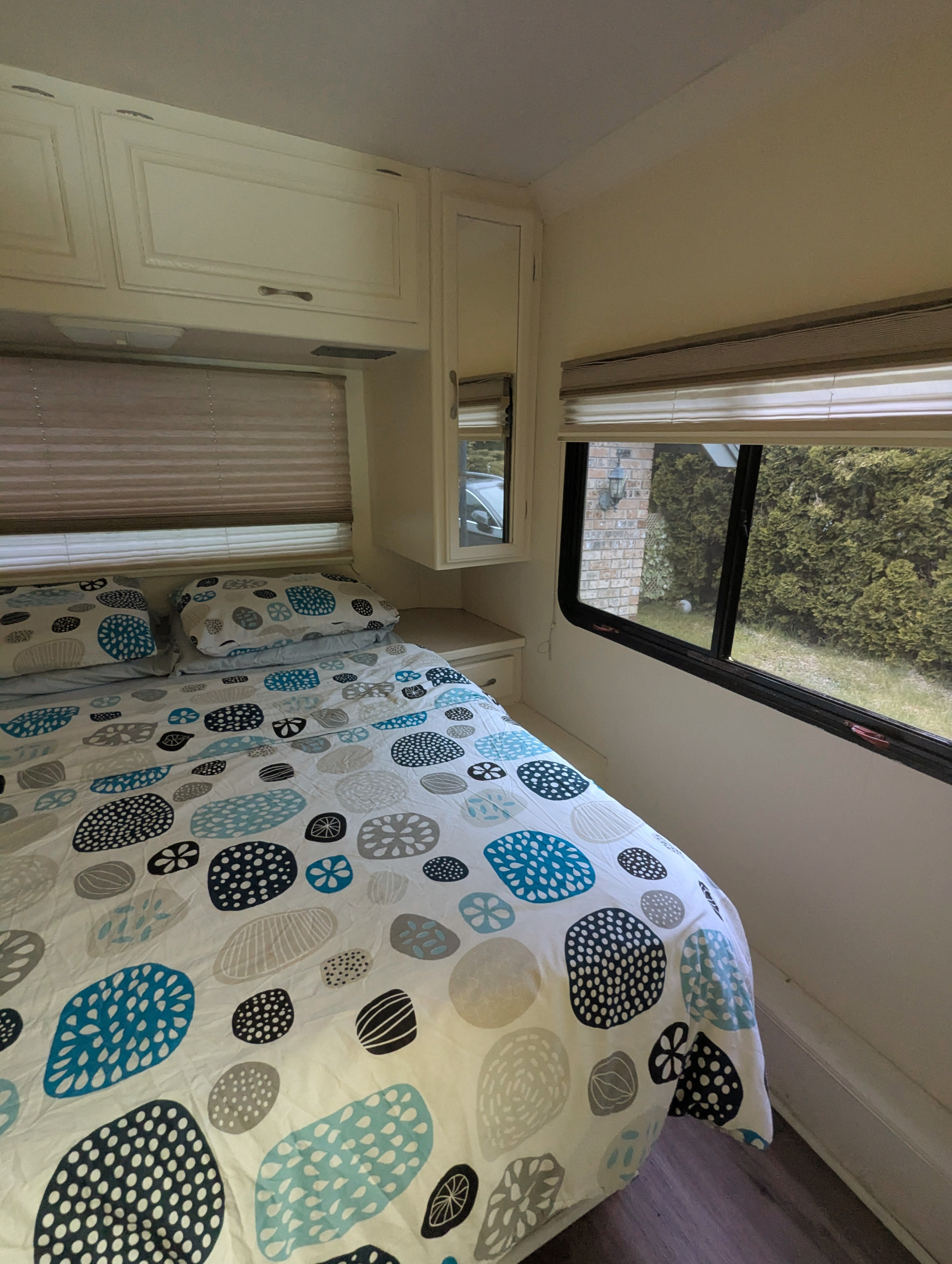 Cozy RV rental bedroom featuring a patterned bed, overhead storage cabinets, and a window overlooking lush greenery.. Four Winds Chateau Sport 2005